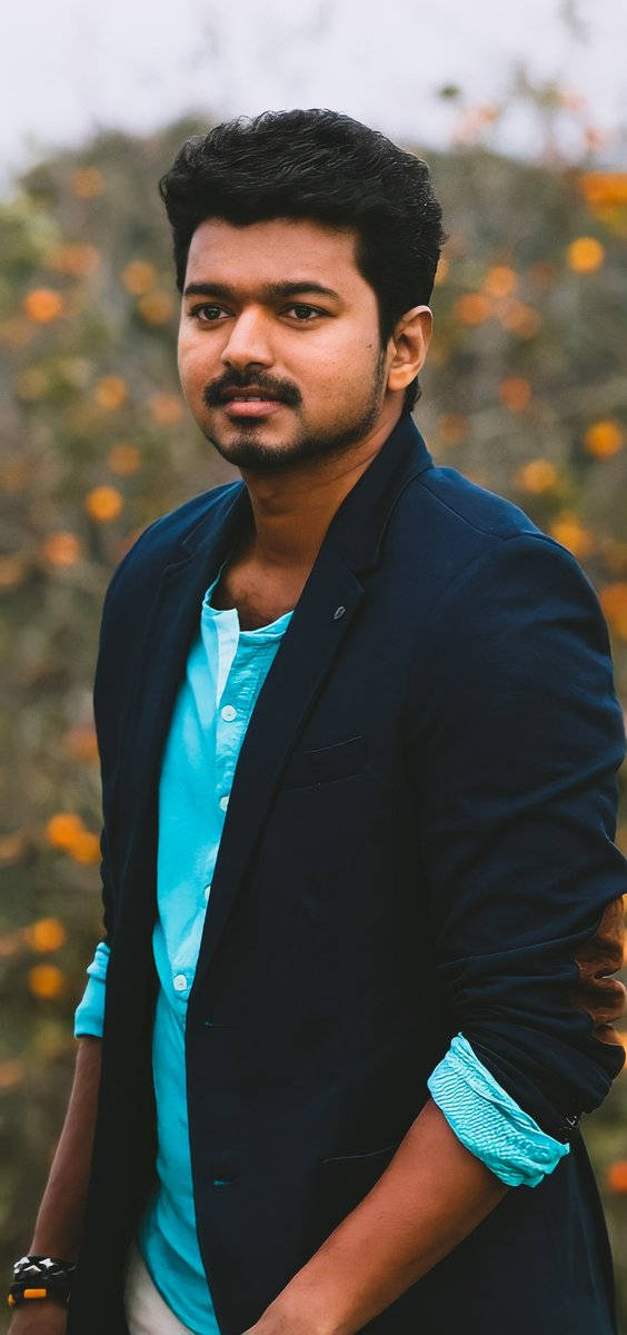 Indian 桌布 壁紙 — 一位留鬍子的年輕男子，身穿海軍藍西裝外套和青綠色襯衫，自信地站在模糊的橙色花朵背景前。