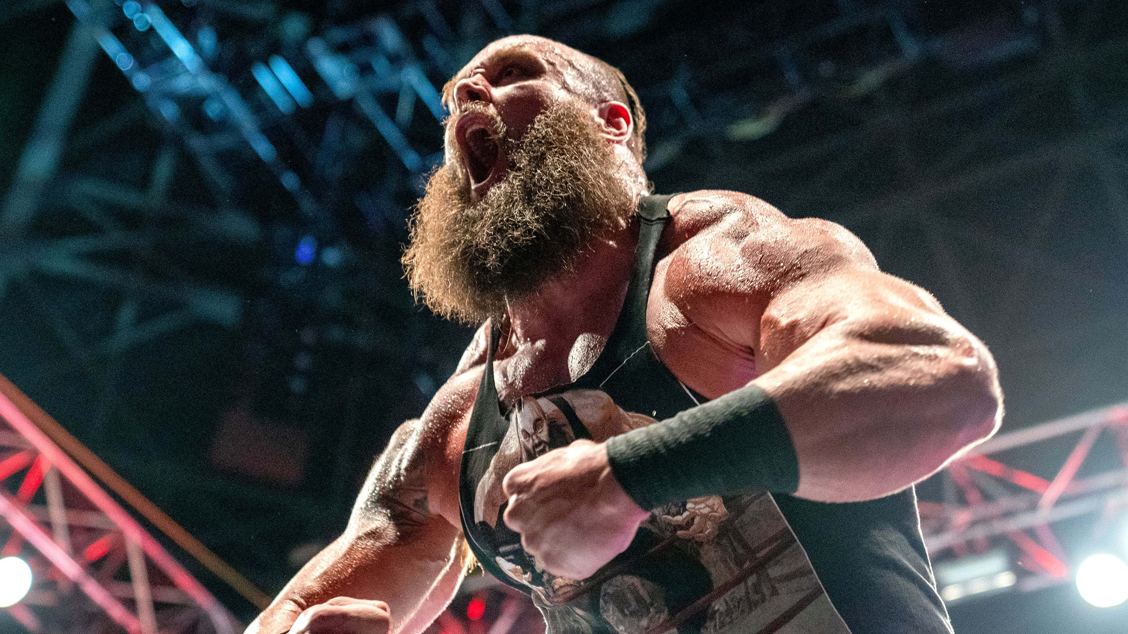 WWE 桌布 壁紙 — 一位留鬍子的摔角手在明亮的場館燈光下，於一場高風險比賽中發出強烈能量的咆哮。