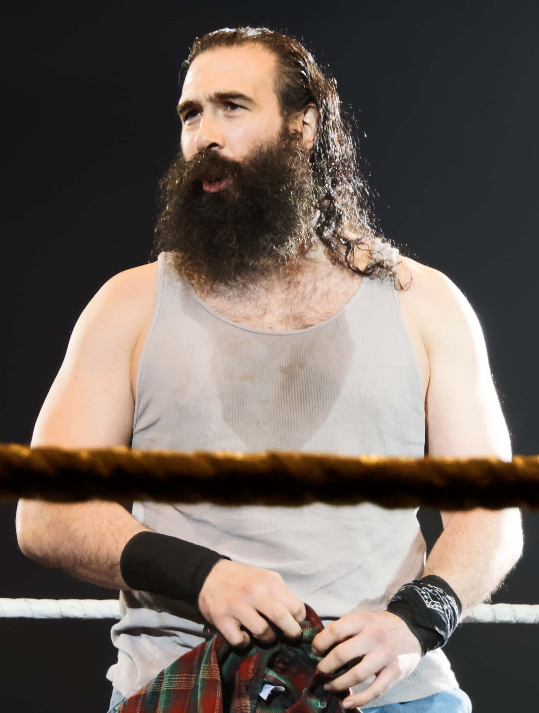 WWE 桌布 壁紙 — 一位留鬍子的摔角手穿著灰色背心，站在摔角擂台內，手持一件格紋襯衫，前景有繩索。