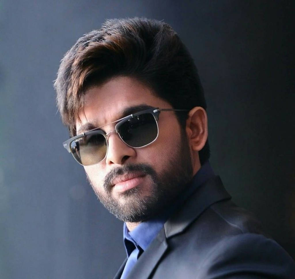 Allu Arjun 桌布 壁紙 — 一位留鬍子的時尚男士，在柔和的灰色背景前戴著時尚太陽眼鏡和深色西裝。