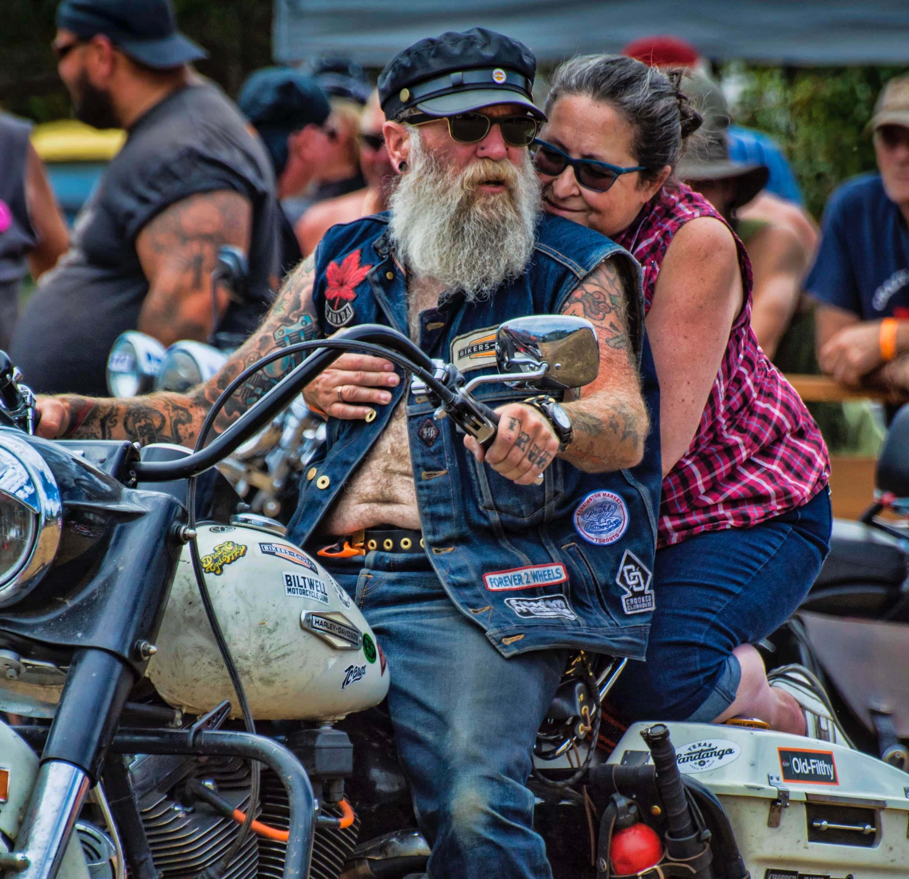 biker 桌布 壁紙 — 一位留鬍子的機車騎士，身上有刺青，穿著牛仔背心，騎著一輛訂製機車，而一位穿著格紋襯衫的女子深情地靠在他的肩膀上。