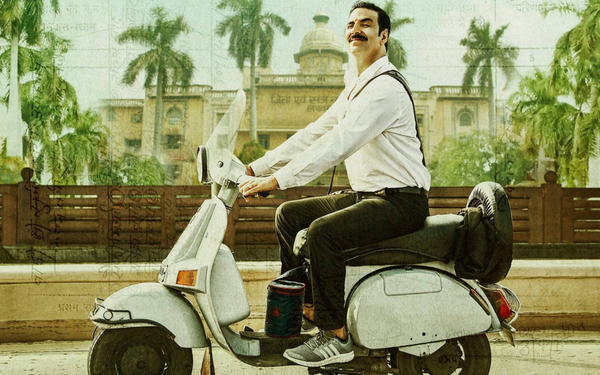 Akshay Kumar 桌布 壁紙 — 一位留鬍子的男人騎著白色滑板車，經過棕櫚樹和殖民風格建築，在明亮的日光下。