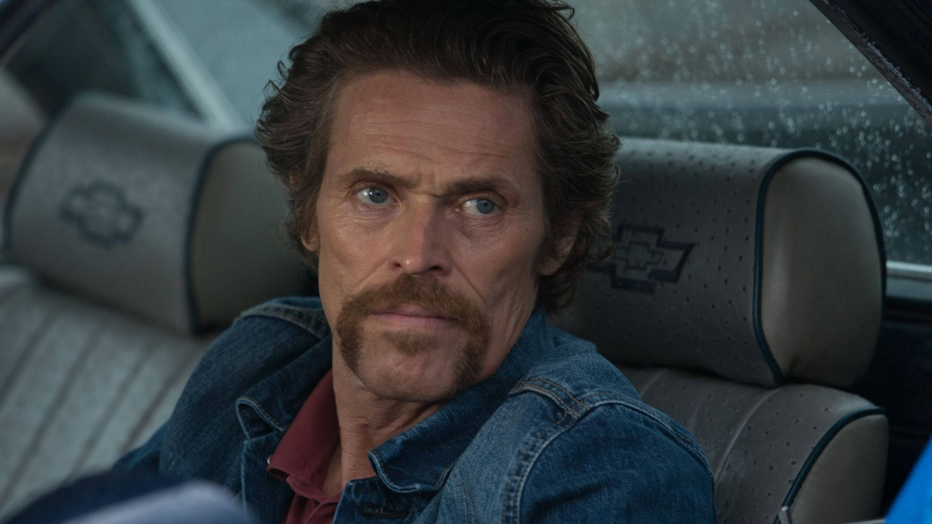 Willem Dafoe 桌布 壁紙 — 一位留鬍子的男士坐在一輛復古車內，雨水在身後的車窗上劃出條紋。