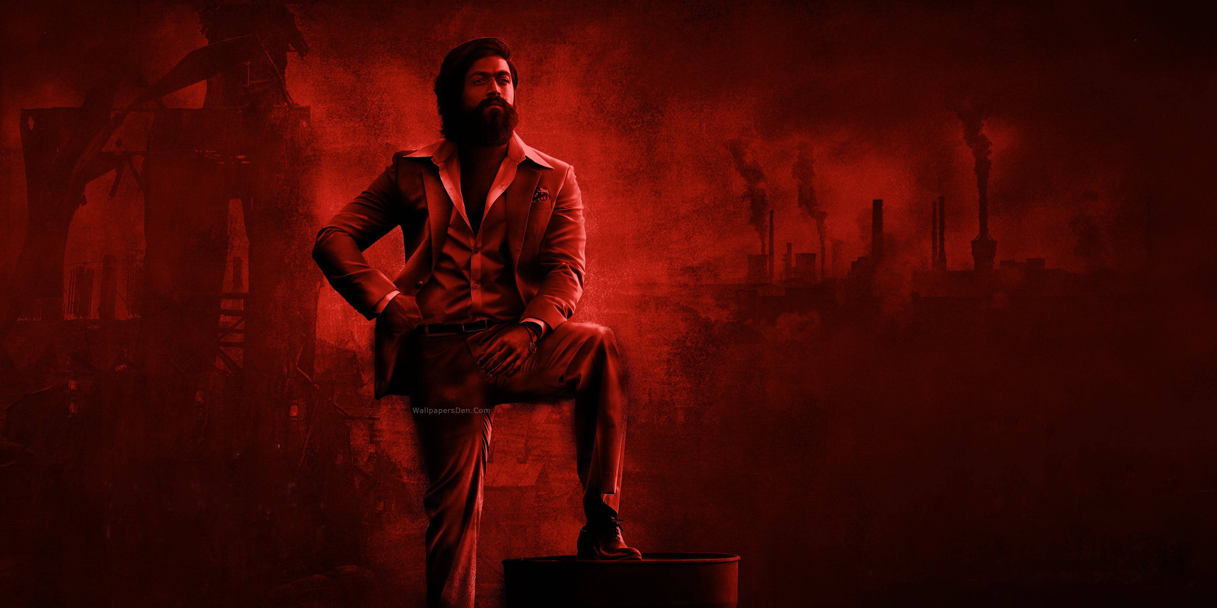 Kgf 2 桌布 壁紙 — 一位留鬍子的男士穿著西裝，自信地坐在一個桶子上，背景是煙霧瀰漫的紅色工業場景，有煙囪。