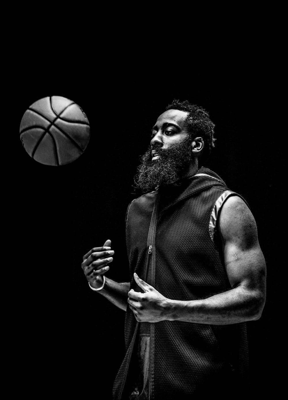 James Harden 桌布 壁紙 — 一位留鬍子的籃球運動員穿著無袖球衣，在戲劇性的黑白背景下，於空中平衡一個籃球。