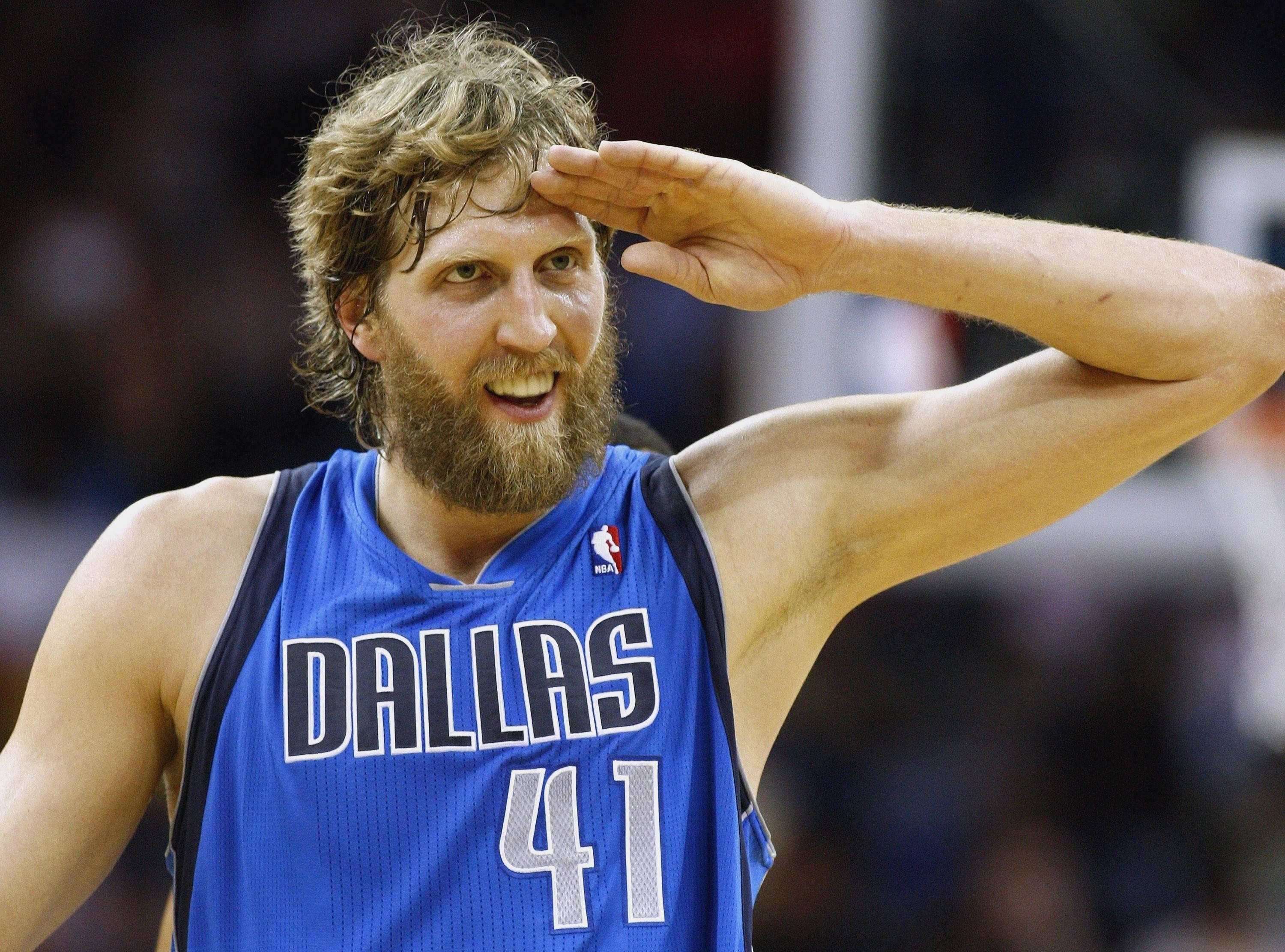 Dirk Nowitzki 桌布 壁紙 — 一位留鬍子的籃球運動員穿著藍色達拉斯球衣，在比賽中咧嘴敬禮。