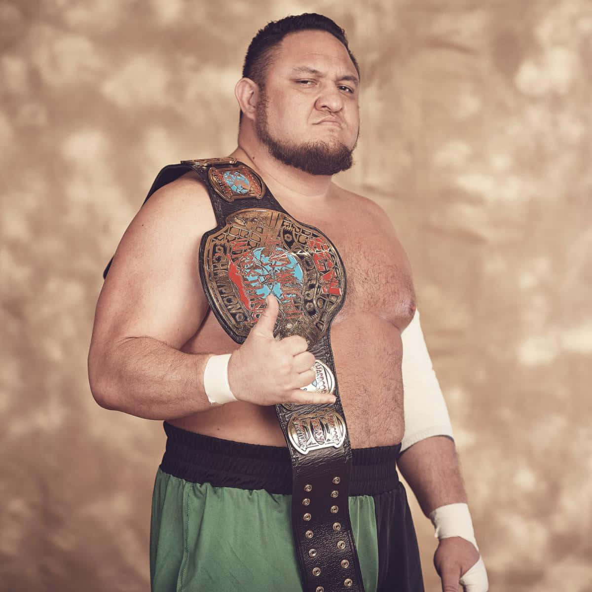 WWE 桌布 壁紙 — 一位留鬍子的肌肉摔角手，戴著冠軍腰帶，在帶有紋理的米色背景前豎起大拇指。