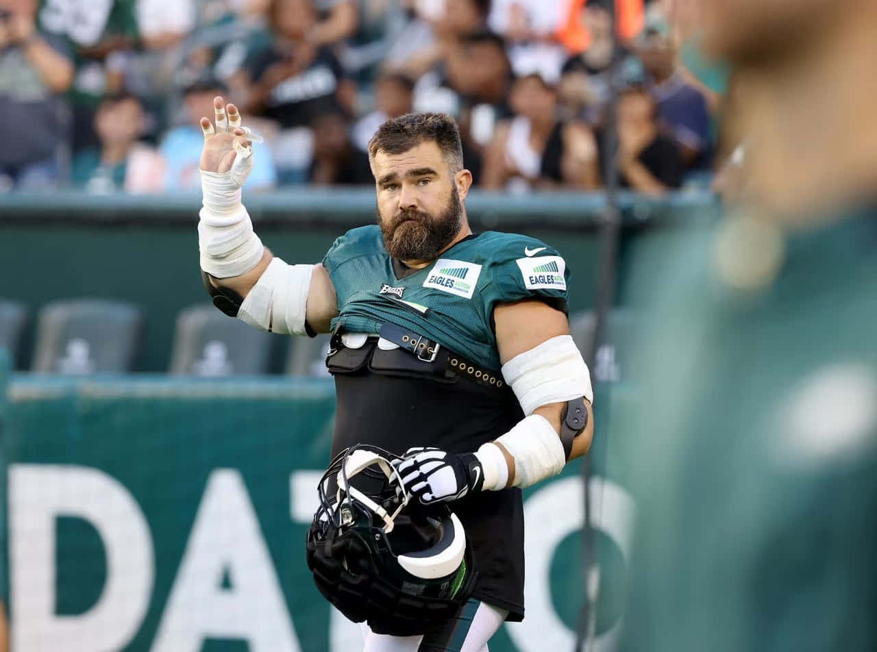 Jason Kelce 桌布 壁紙 — 一位留鬍子的費城老鷹隊美式足球員，身穿綠色球衣，在日間比賽中向球迷揮手，同時拿著頭盔。