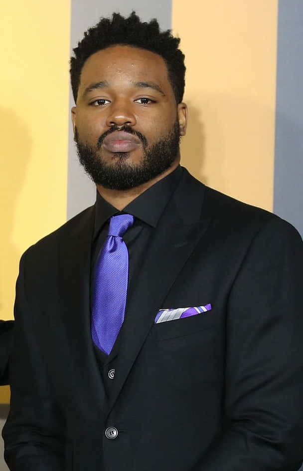 Ryan Coogler 桌布 壁紙 — 一位留鬍子短髮的男子穿著黑色西裝，搭配鮮紫色領帶，背景是黃色和灰色條紋。