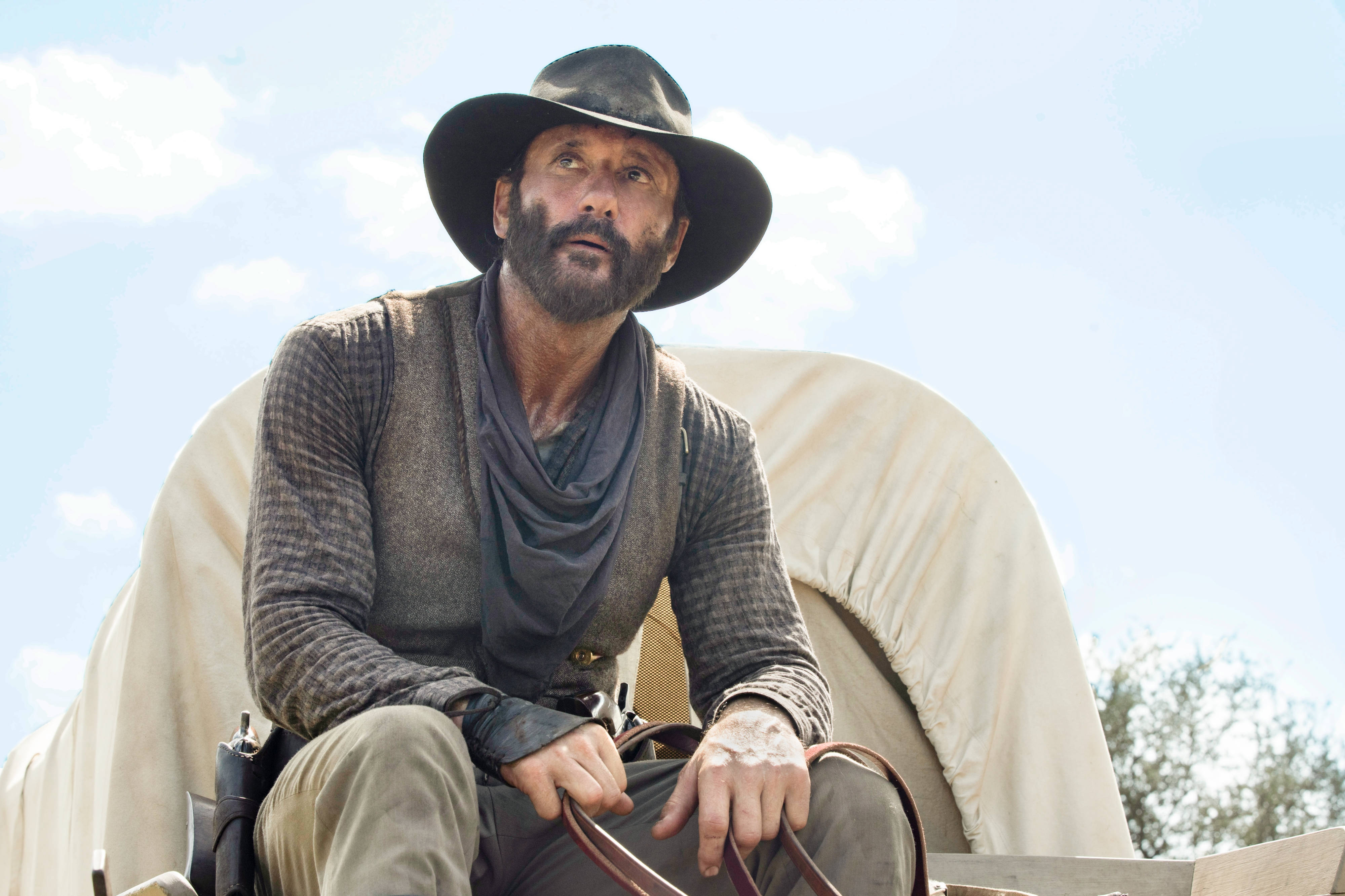 Tim Mcgraw 桌布 壁紙 — 一位留鬍鬚、戴寬邊帽的男人坐在有篷馬車上，頭頂是晴朗藍天，點綴著幾朵白雲。