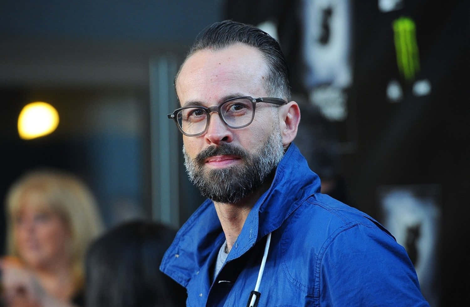 Jason Lee 桌布 壁紙 — 一位留鬍鬚、戴眼鏡的男人，穿著藍色外套，在昏暗的室內環境中看著相機。