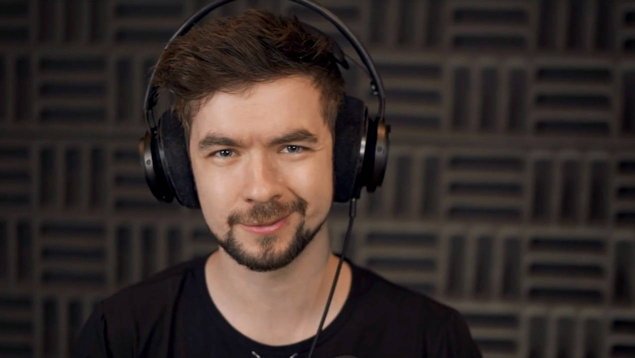 Jacksepticeye 桌布 壁紙 — 一位留鬍鬚、戴耳機的男子在深色隔音板牆前對著鏡頭微笑。
