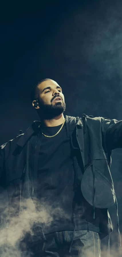 Aesthetic Drake 桌布 壁紙 — 一位留鬍鬚、戴耳機的男表演者站在煙霧瀰漫的舞台上，在戲劇性燈光下雙臂伸展。