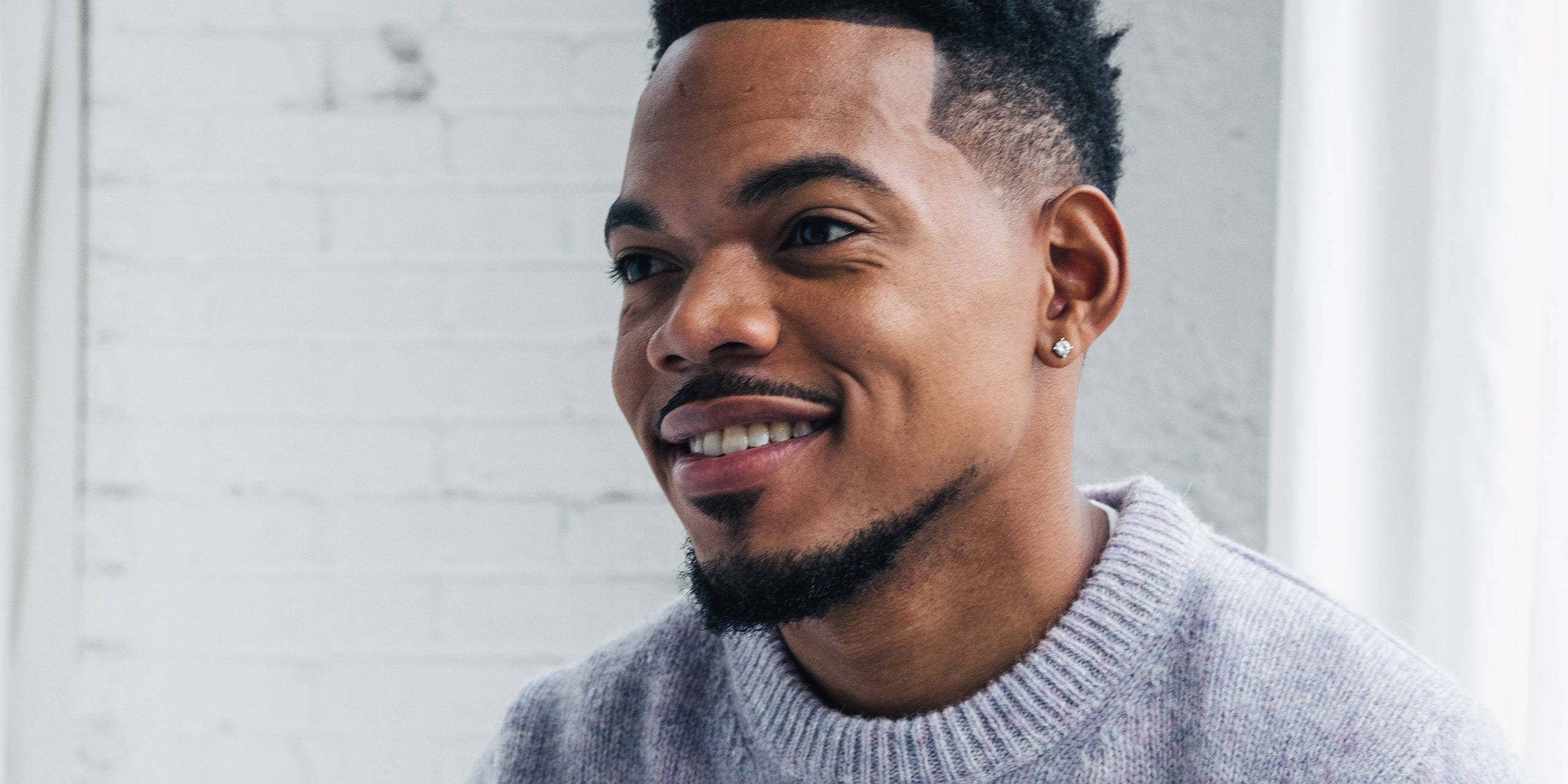 chance 桌布 壁紙 — 一位留鬍鬚、戴耳環的微笑男士，身穿灰色毛衣，背景是白色磚牆。