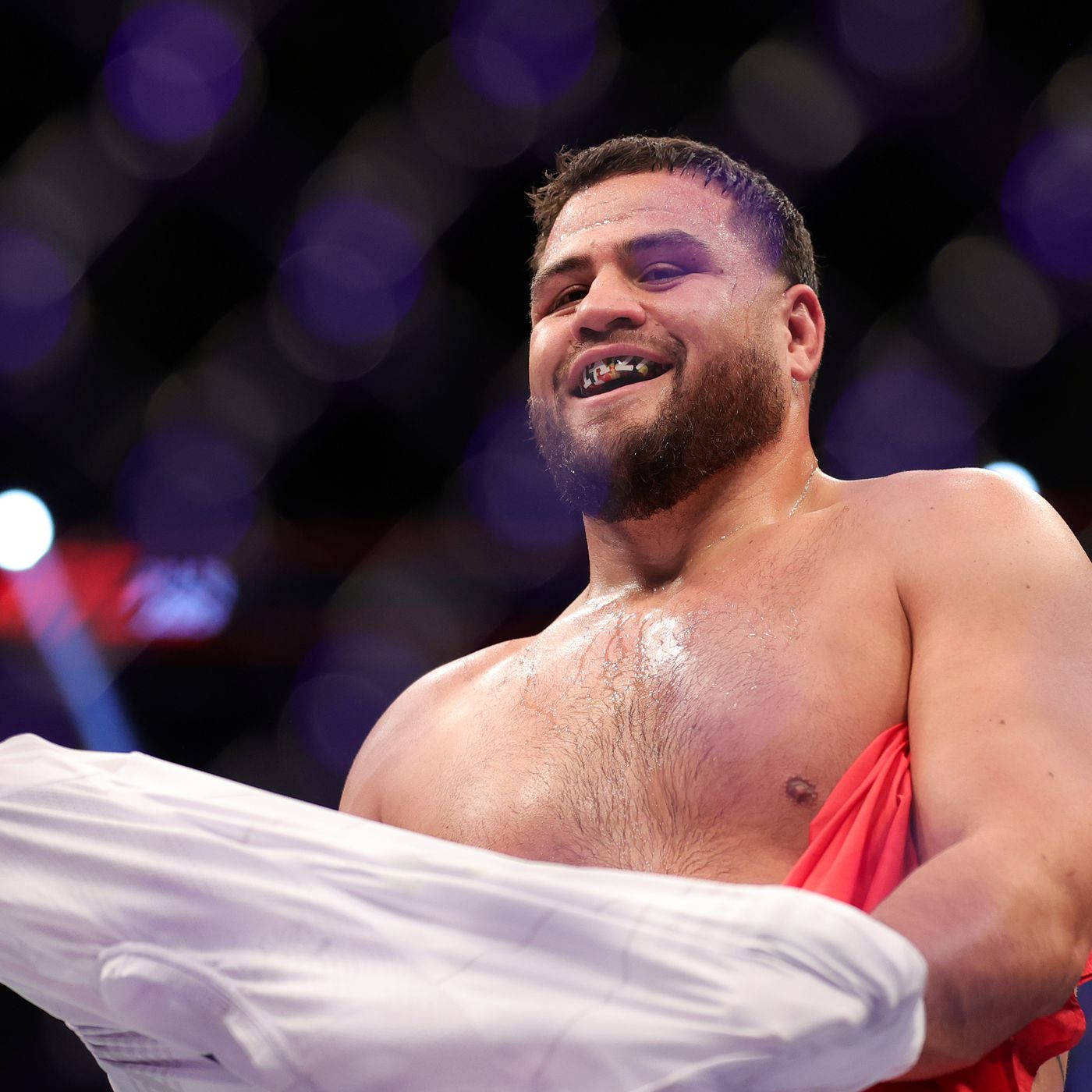 UFC 桌布 壁紙 — 一位留鬍鬚、戴護齒的勝利拳擊手在擂台上舉起白色短褲，笑容燦爛。