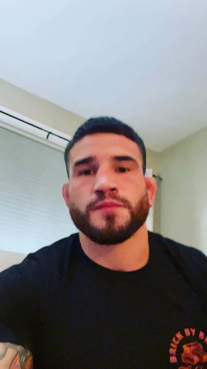 Athlete 桌布 壁紙 — 一位留鬍鬚、手臂有刺青的男士在柔和光線的室內直視鏡頭。