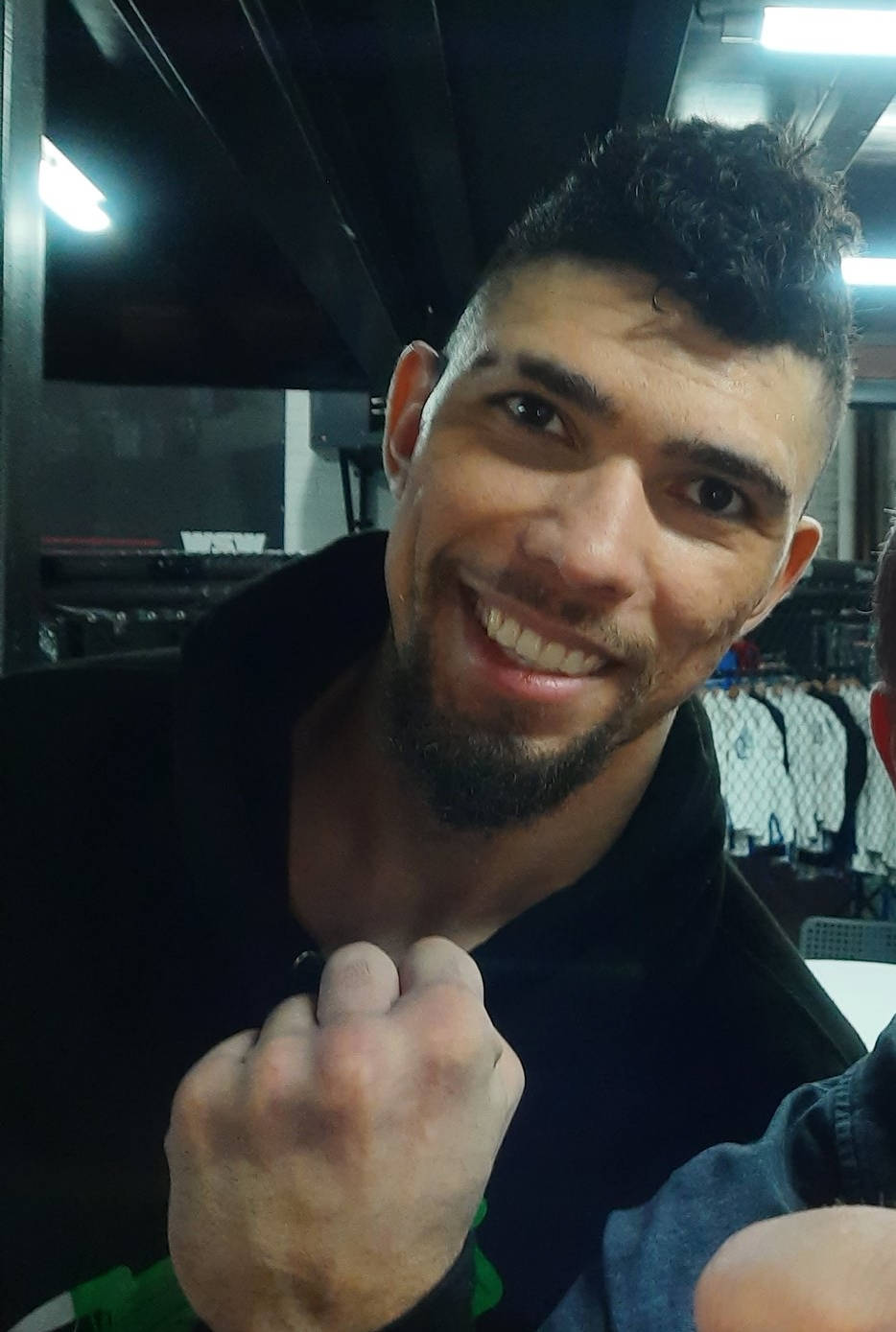 smiling 桌布 壁紙 — 一位留鬍鬚、捲髮的男子在燈光昏暗的健身房裡握緊拳頭擺姿勢微笑。