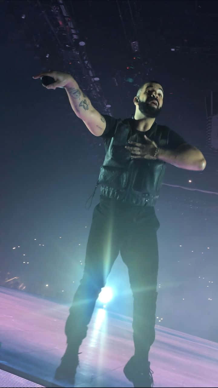 Drake 桌布 壁紙 — 一位留鬍鬚、有刺青的男士在昏暗的舞台上，在明亮的聚光燈和煙霧效果下表演。