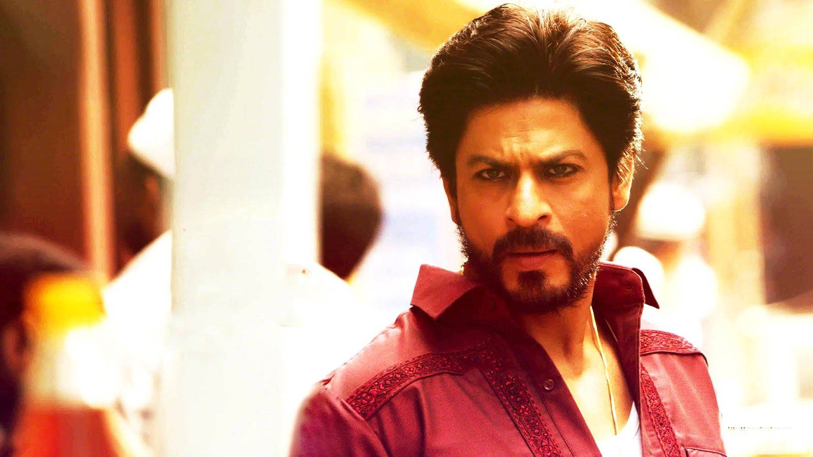 Shahrukh 桌布 壁紙 — 一位留鬍鬚、眼神銳利的男士，穿著紅色刺繡襯衫，背景是溫暖燈光的城市景觀。
