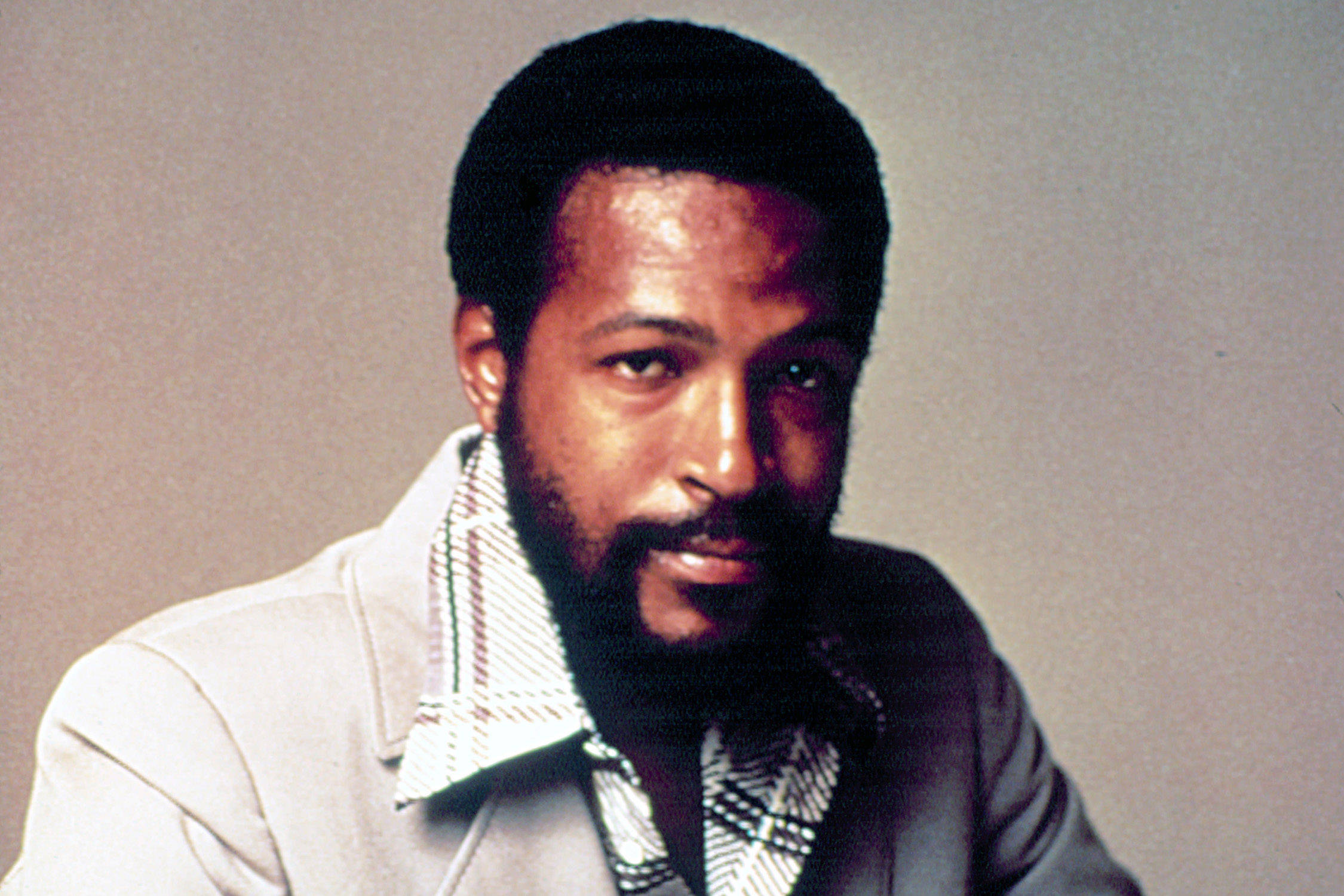Marvin Gaye 桌布 壁紙 — 一位留鬍鬚、短髮的男子，在純色工作室背景前，穿著輕便外套搭配圖案襯衫。