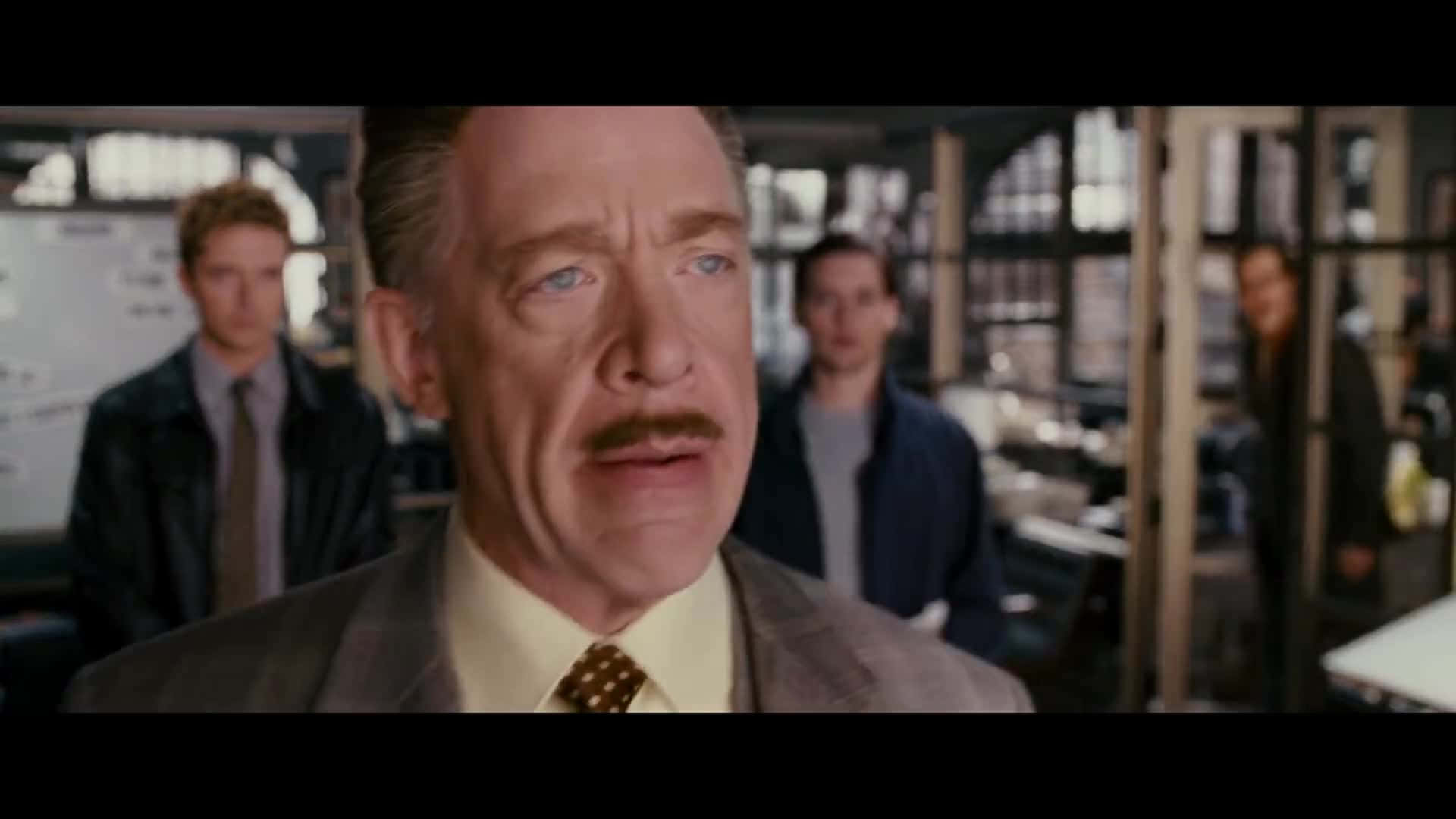 J Jonah Jameson 桌布 壁紙 — 一位留鬍鬚、穿西裝的男人在辦公室裡顯得驚訝，背景有模糊的同事。