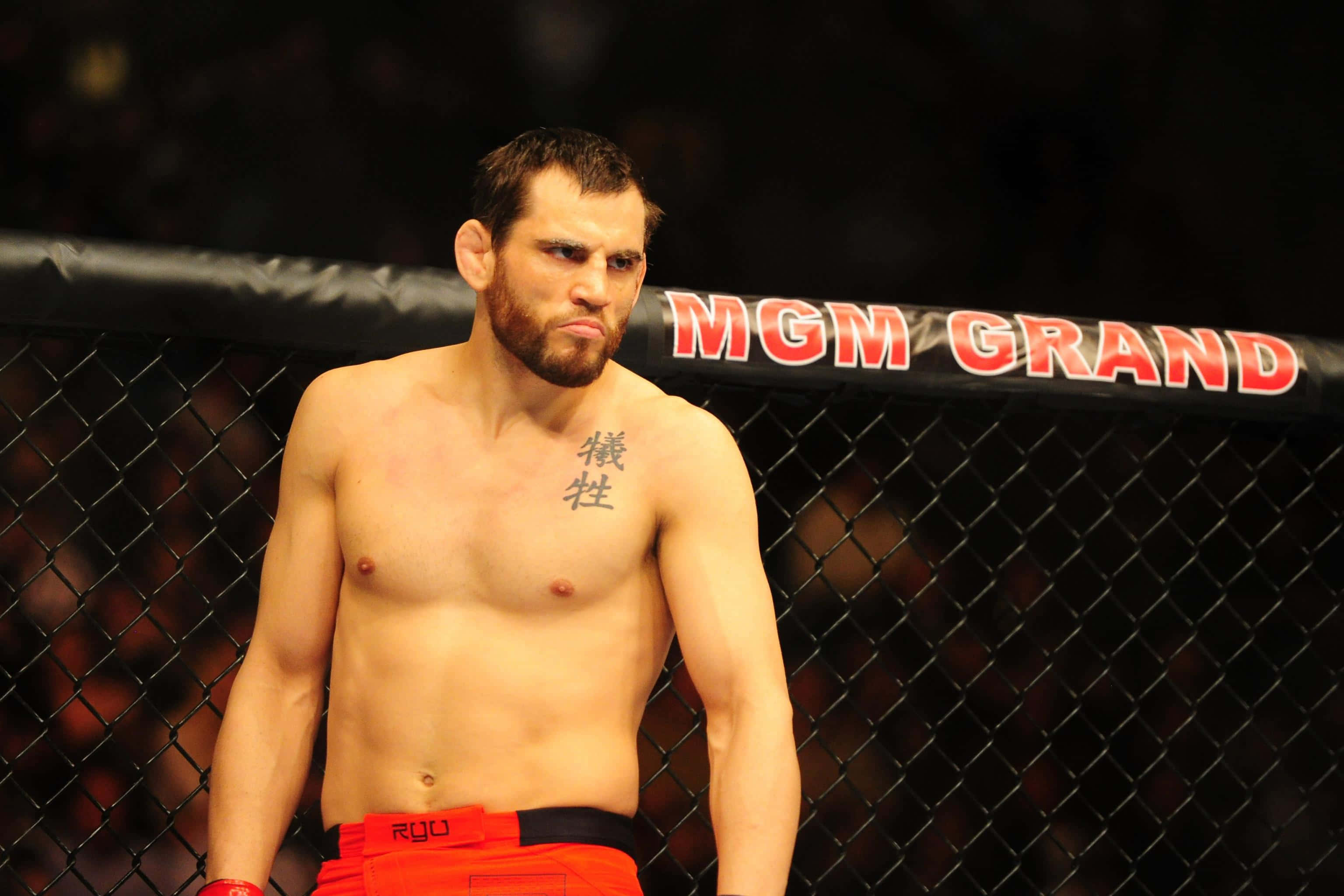 UFC 桌布 壁紙 — 一位留鬍鬚、胸前有刺青的肌肉戰士，在MGM Grand的場館燈光下站在MMA籠內。