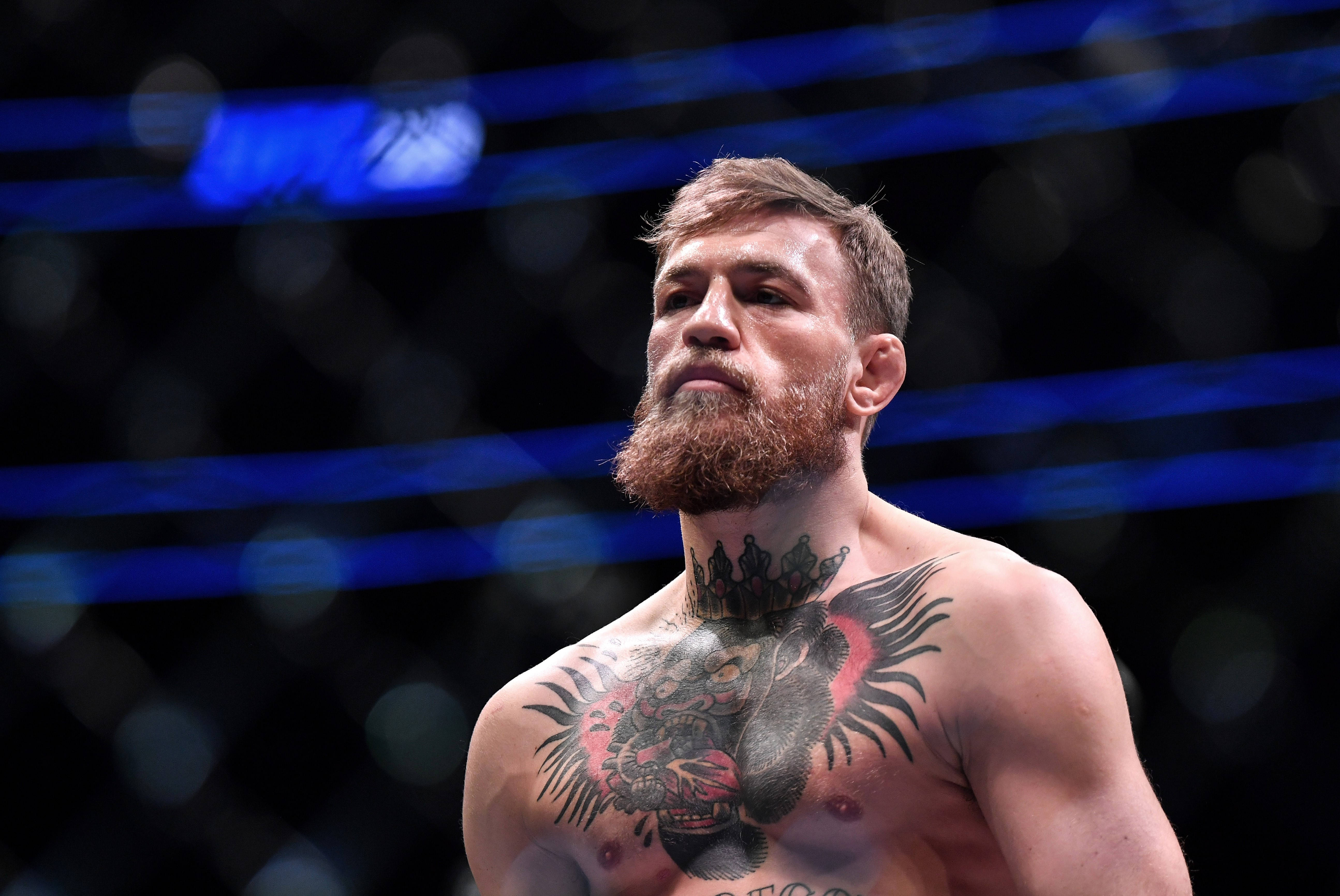 UFC 桌布 壁紙 — 一位留鬍鬚、胸口有刺青的戰士，站在藍色燈光的八角籠內，在競技場燈光下專注而激烈。