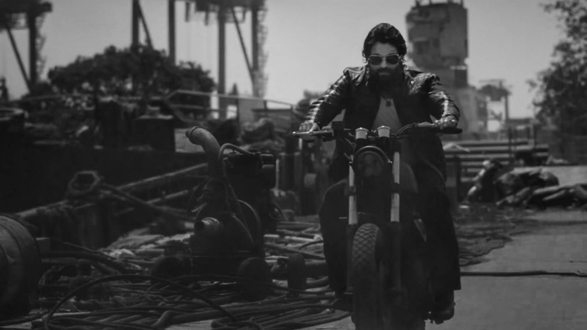 留鬍鬚和戴太陽眼鏡的男人騎摩托車穿過工業廢車場。