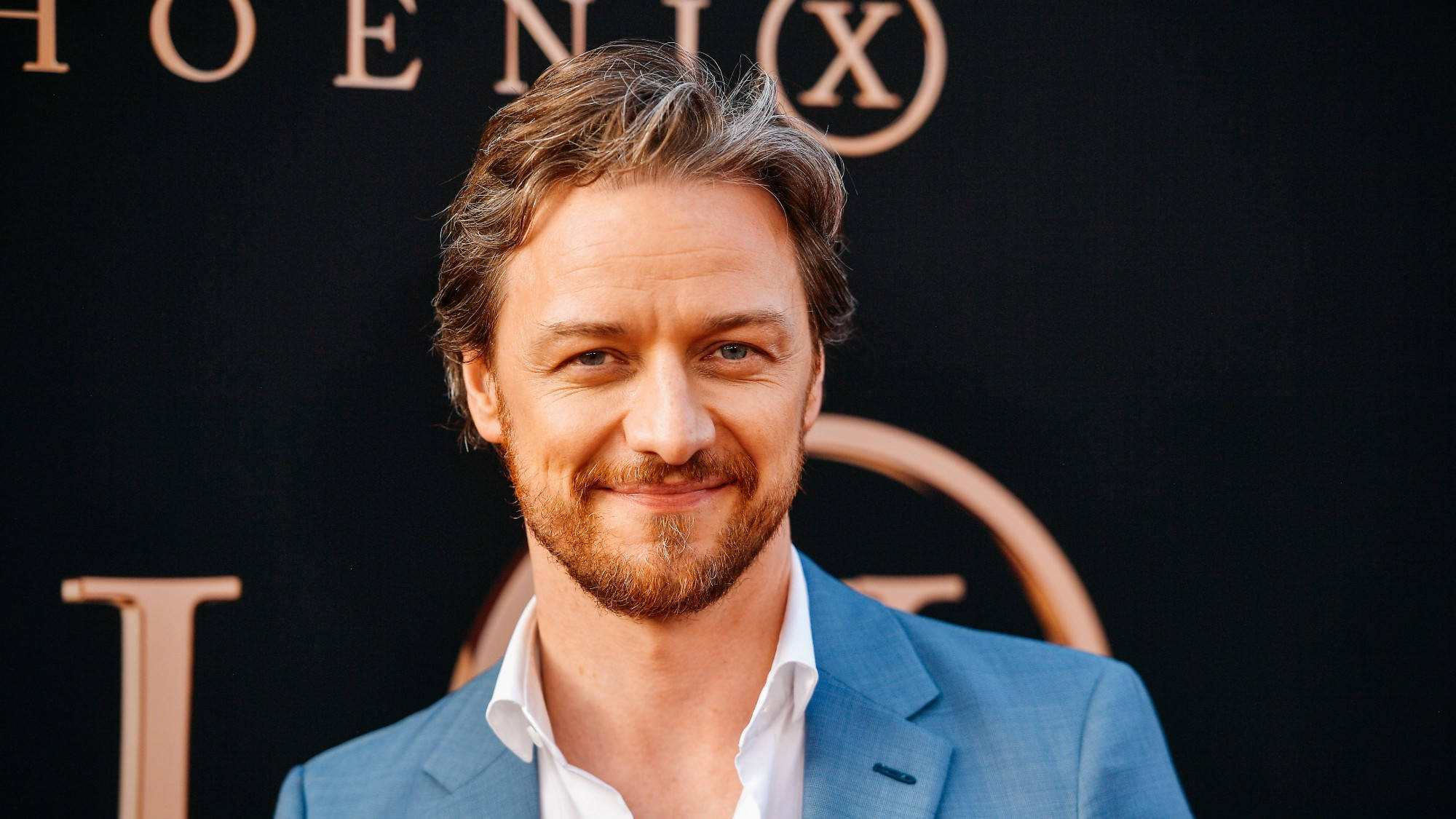 Celebrity 桌布 壁紙 — 一位留鬍鬚、面帶微笑的男子身穿藍色西裝，站在帶有金色字樣的黑色背景前。