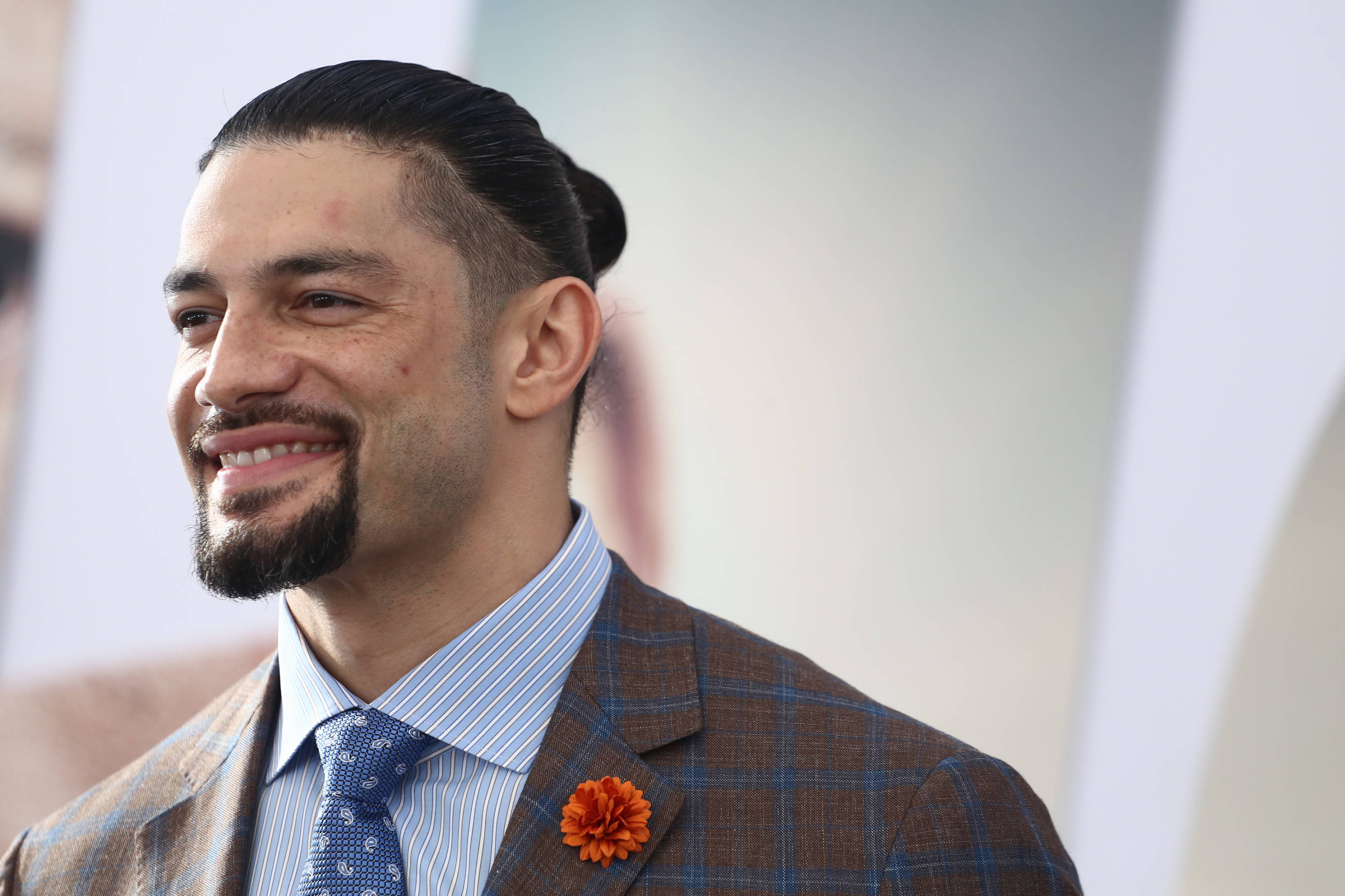 Roman 桌布 壁紙 — 一位留鬍鬚、頭髮向後梳的微笑男士，穿著格紋西裝，搭配藍色領帶和橙色襟花。