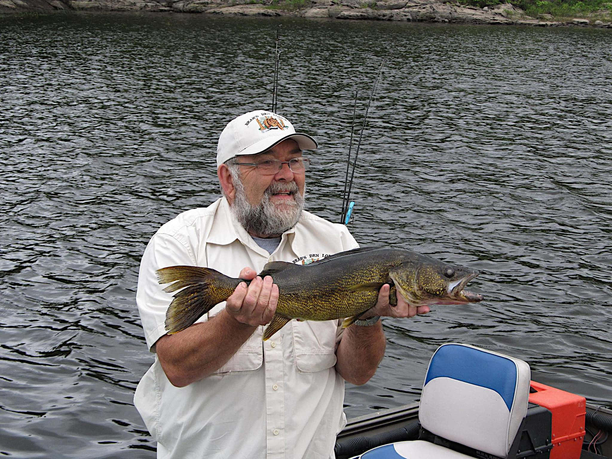 Walleye 桌布 壁紙 — 一位留鬍鬚戴帽子的年長男子，自豪地抱著他在平靜湖面上從船上釣到的一條大梭鱸。