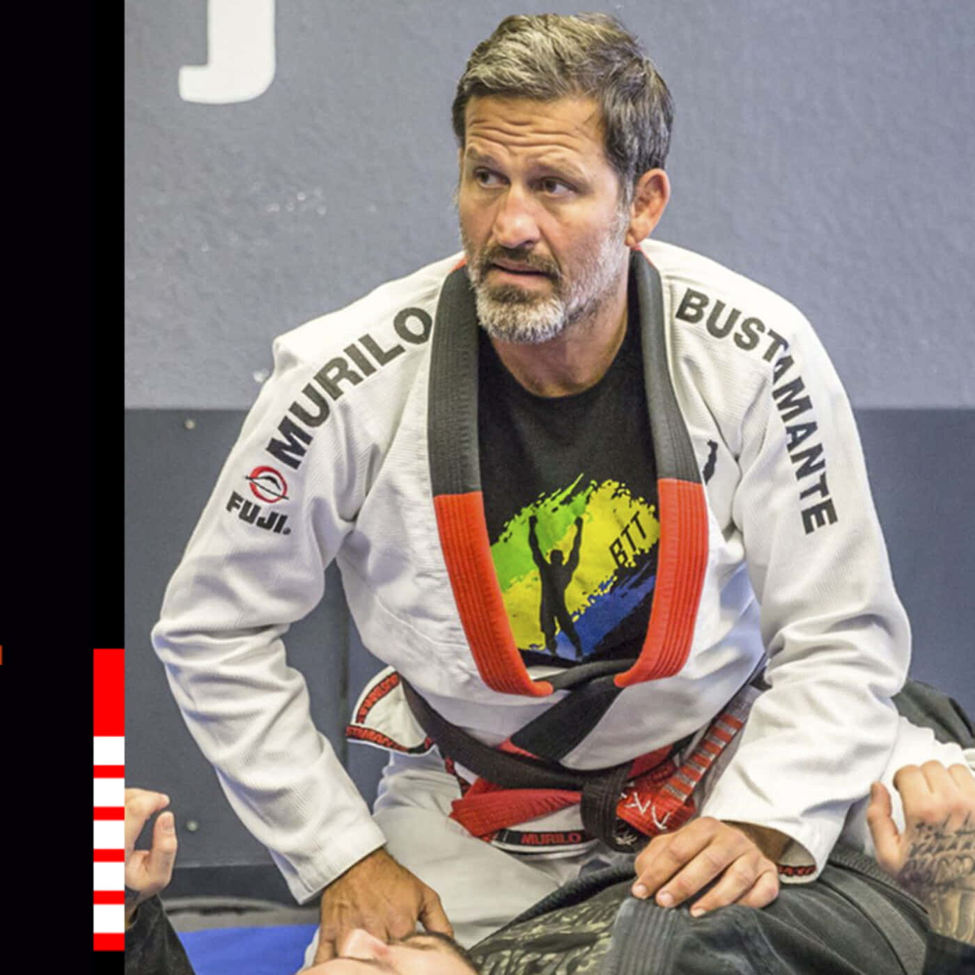 MMA 桌布 壁紙 — 一位留鬍鬚的中年男子專注地穿著白色巴西柔術道服，繫著紅黑腰帶，坐在墊子上。