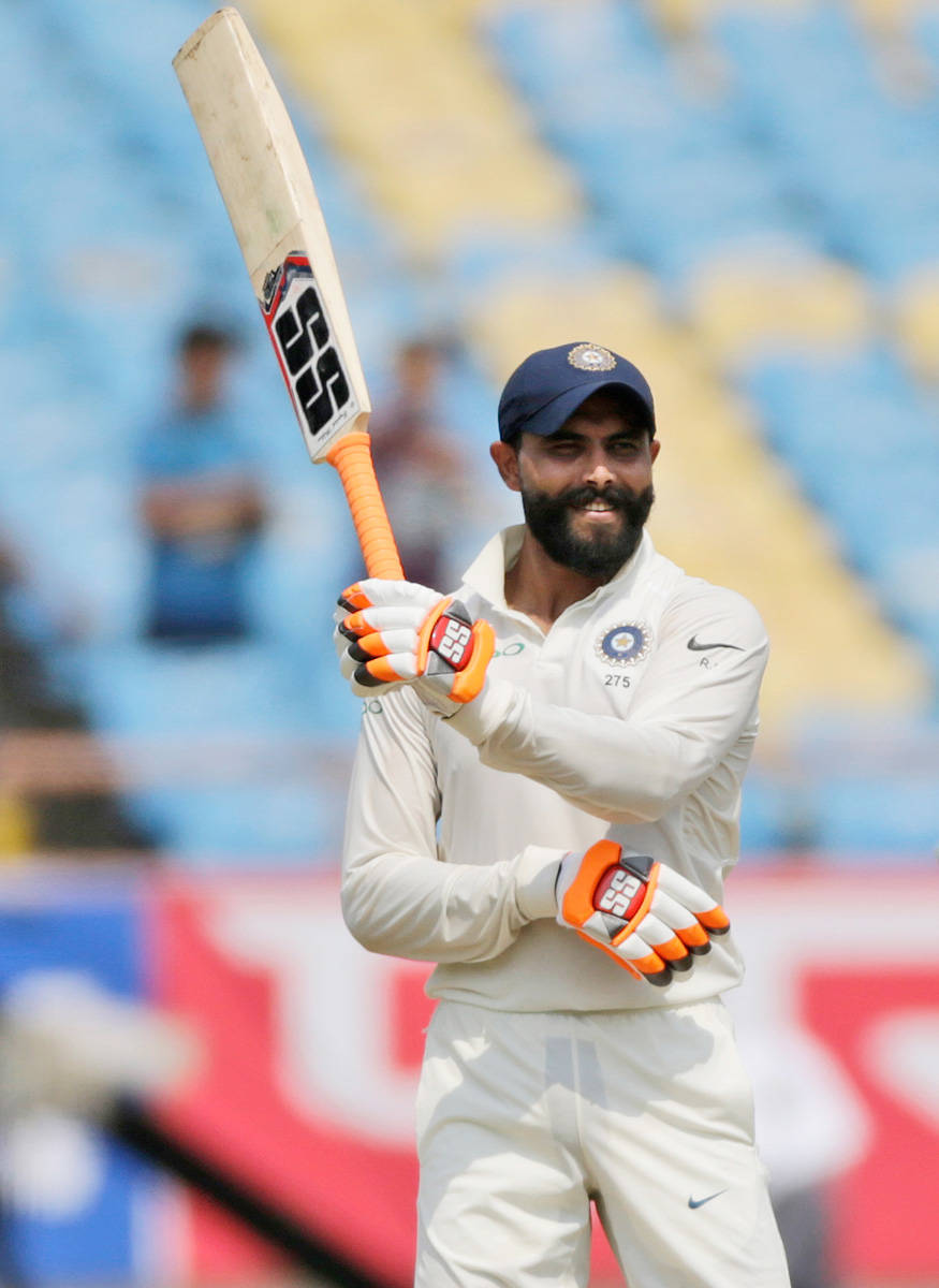 運動 桌布 壁紙 — 一位留鬍鬚的印度板球運動員身穿白色制服，在陽光明媚的球場上自信微笑，高舉球棒。