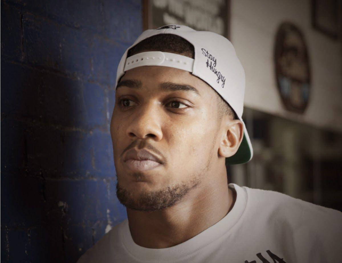Anthony Joshua 桌布 壁紙 — 一位留鬍鬚的年輕男子戴著白色帽子，上面寫著「Stay Hungry」，靠著紋理藍色磚牆。