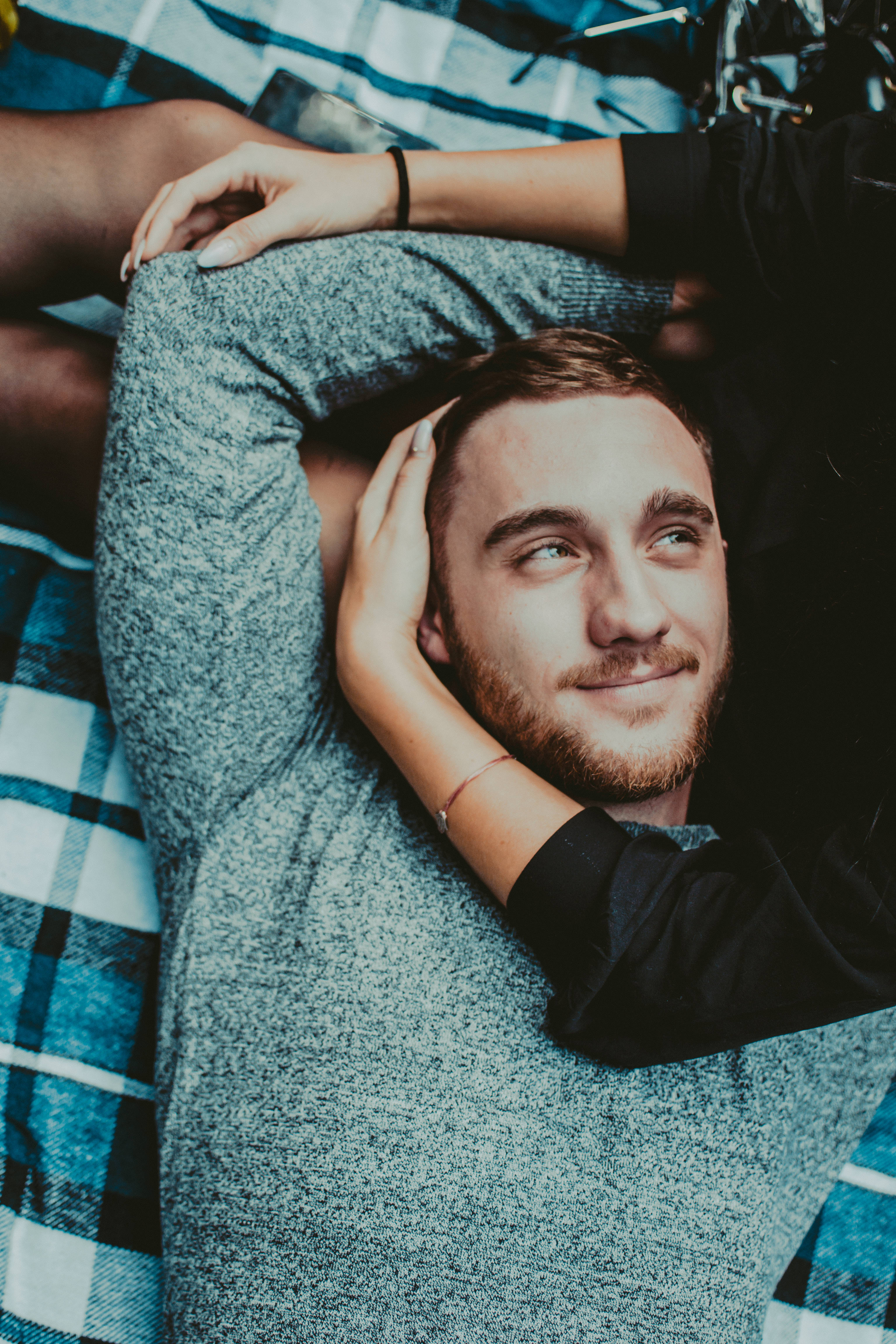 Love And Friendship 桌布 壁紙 — 一位留鬍鬚的年輕男子放鬆地躺在藍色格紋毯上，雙手輕輕托著頭部，露出溫柔的微笑。