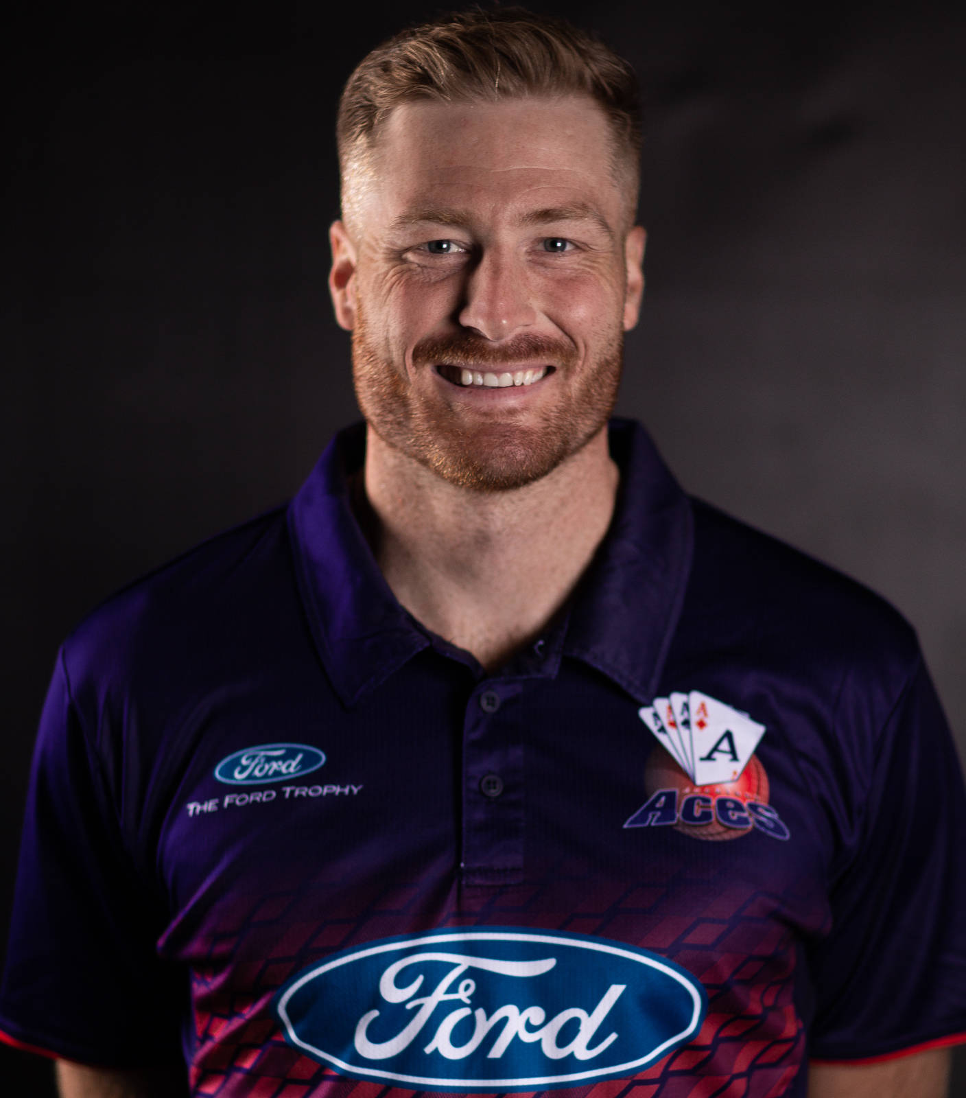 martin guptill 桌布 壁紙 — 一位留鬍鬚的微笑男士穿著紫色Ford Trophy Polo衫，上面有四個A的標誌，背景是深色攝影棚。