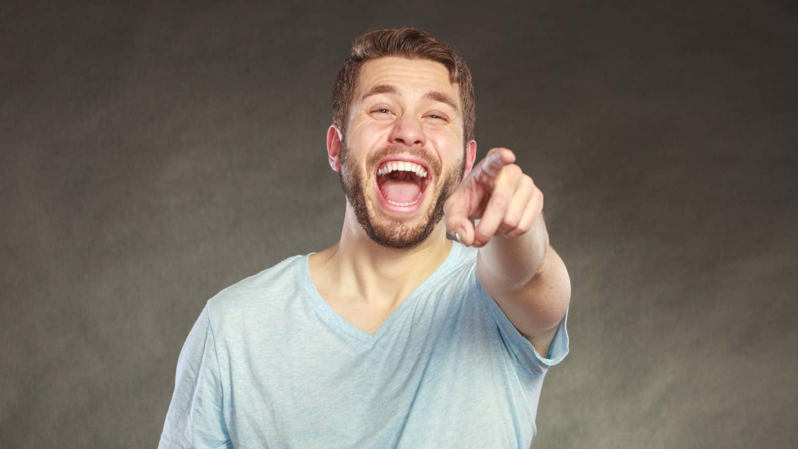 Laughing 桌布 壁紙 — 一位留鬍鬚的快樂男士在柔和的灰色背景前，開懷大笑並直接指向觀眾。