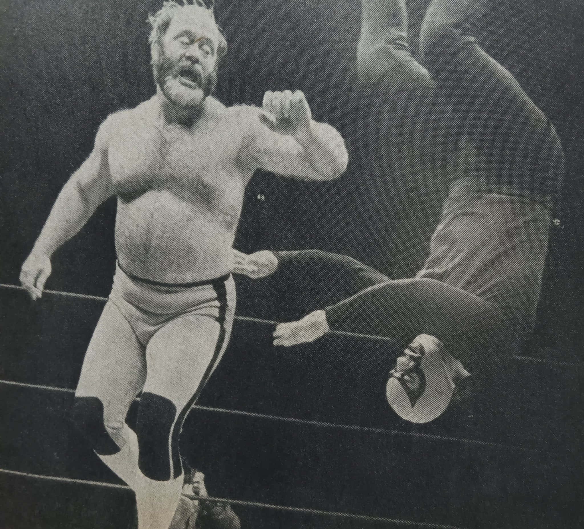 WWE 桌布 壁紙 — 一位留鬍鬚的摔角手穿著緊身褲，跳過倒下的對手，這是一張復古黑白摔角場照片。