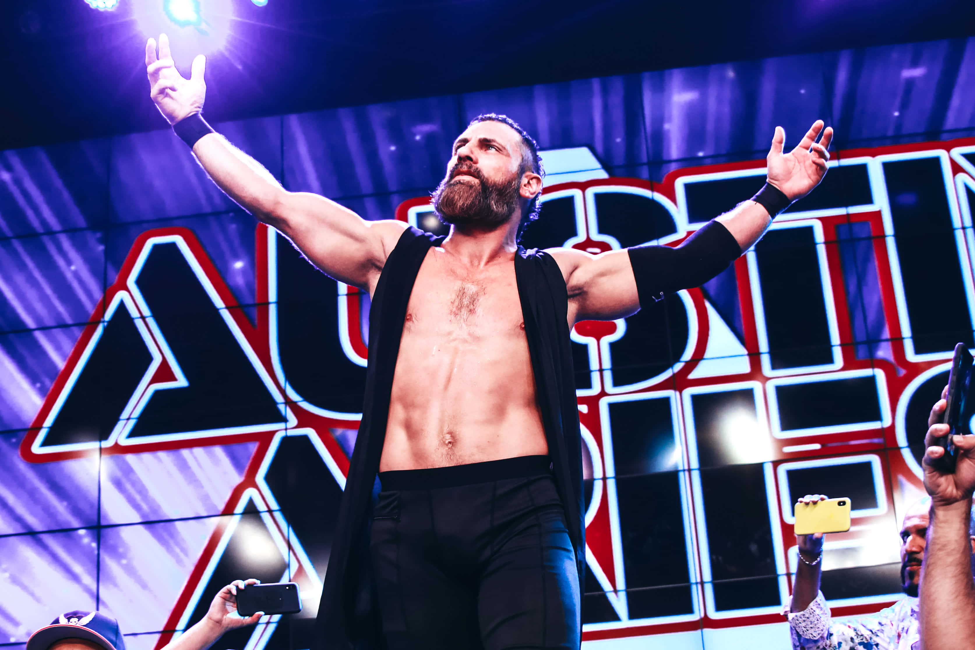 WWE 桌布 壁紙 — 一位留鬍鬚的摔角手穿著黑色三角褲和開襟背心，在紫色舞台燈光下高舉雙臂，背景寫著 'AUSTIN'。