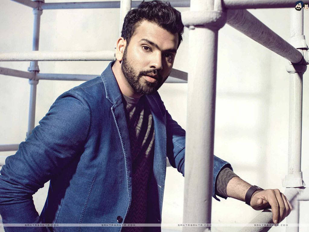 Rohit Sharma 桌布 壁紙 — 一位留鬍鬚的時尚男士在明亮的工業環境中靠著白色管道，身穿藍色外套。