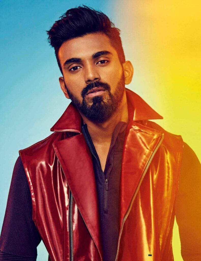 kl rahul 桌布 壁紙 — 一位留鬍鬚的時尚男士穿著閃亮的紅色皮背心，背景是充滿活力的藍色和黃色漸變色。