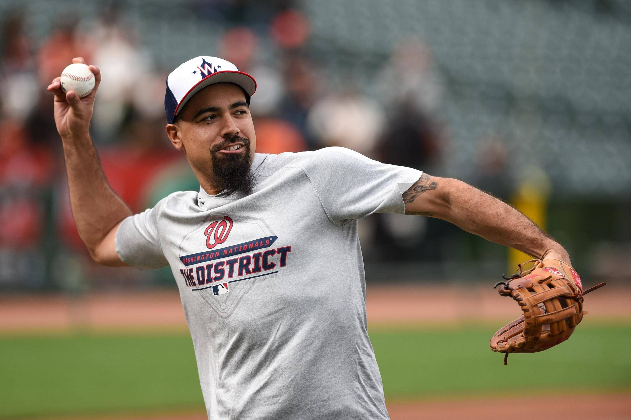 anthony rendon 桌布 壁紙 — 一位留鬍鬚的棒球投手，身穿華盛頓國民隊球衣，在陽光普照的球場上準備投球。