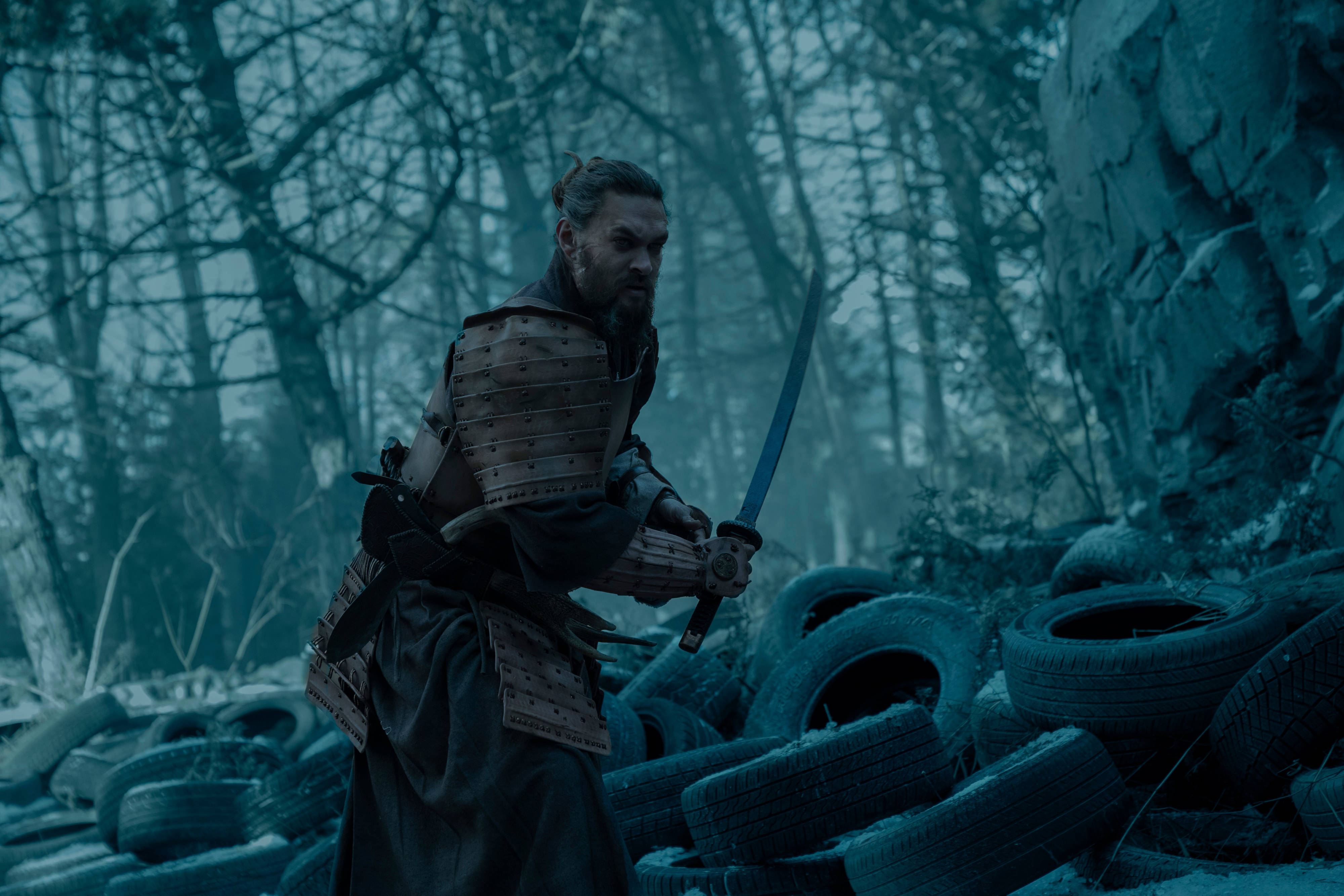 jason 桌布 壁紙 — 一位留鬍鬚的武士身穿鎧甲，在陰暗的森林中手持武士刀，森林裡散落著廢棄輪胎。