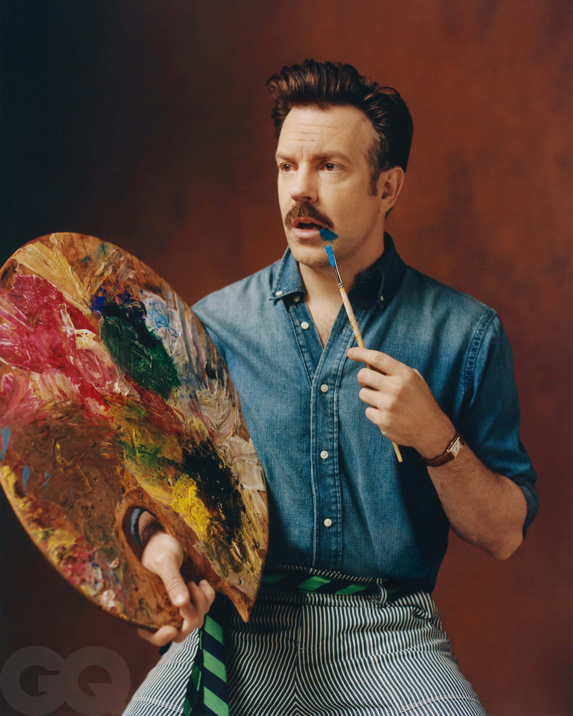 jason sudeikis 桌布 壁紙 — 一位留鬍鬚的男人在暖棕色背景前，拿著一個調色盤和一支畫筆，嘴唇上沾了藍色顏料。