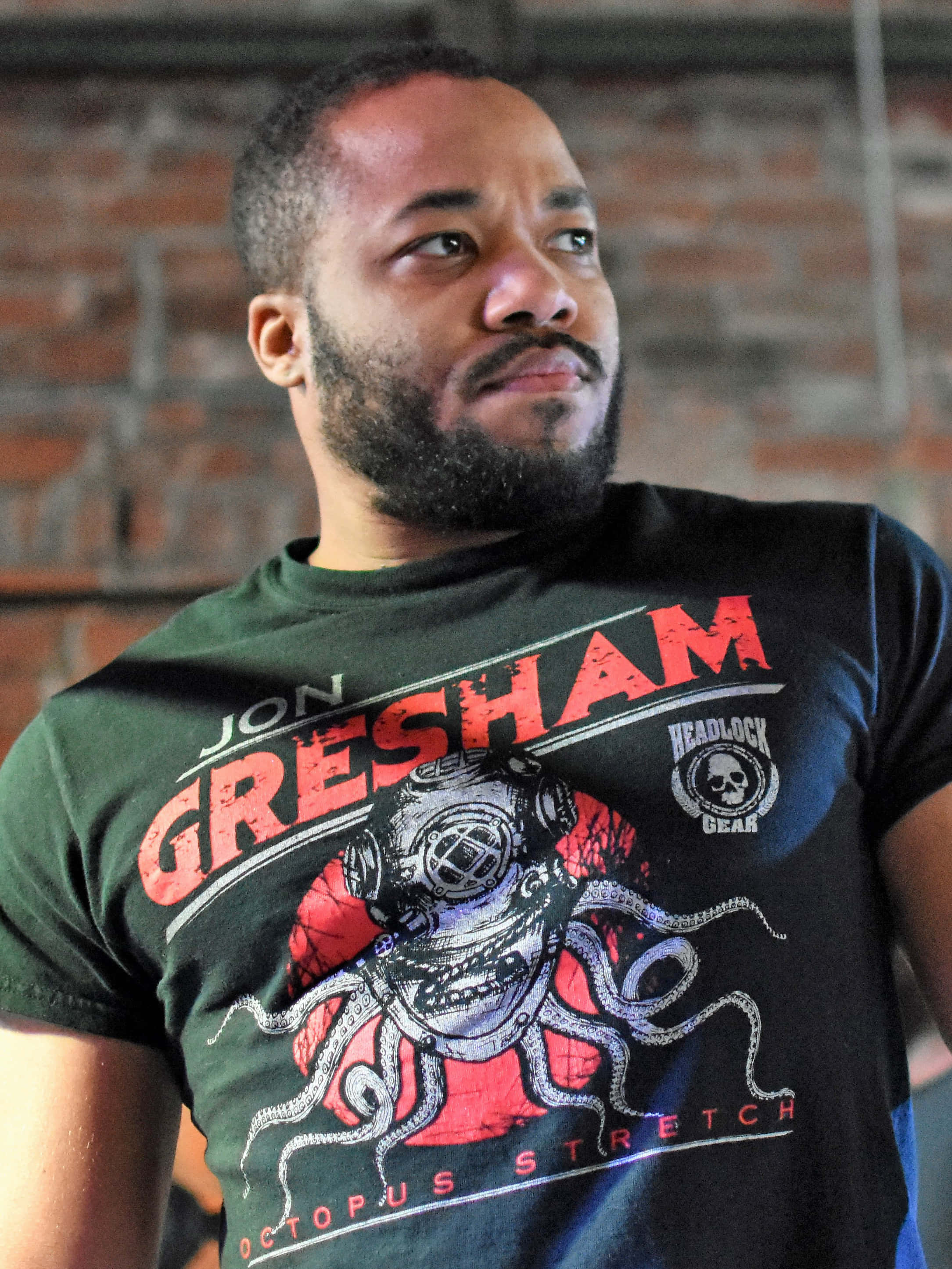 Jonathan 桌布 壁紙 — 一位留鬍鬚的男人穿著一件印有章魚和 'Jon Gresham' 文字的圖案T恤，背景是磚牆。