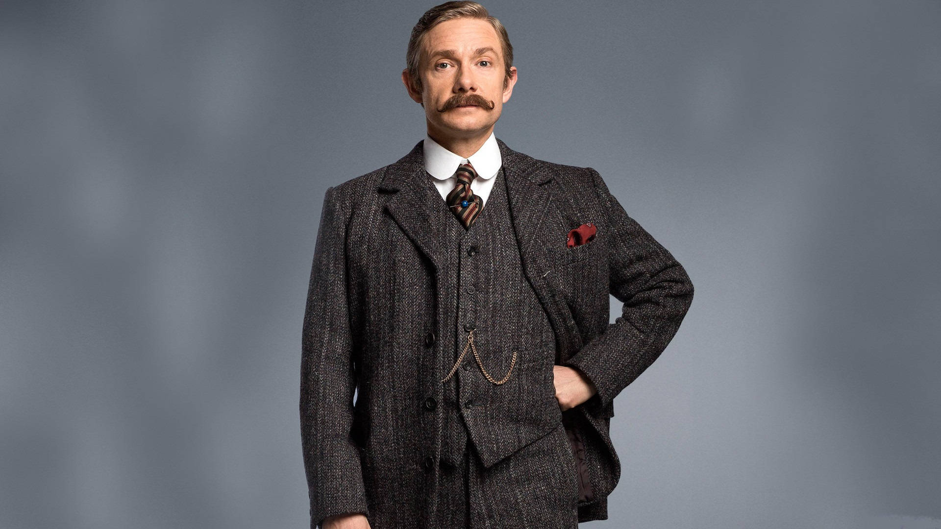Martin Freeman 桌布 壁紙 — 一位留鬍鬚的男人穿著質感灰色三件套西裝，搭配紅色口袋方巾，背景為柔和的灰色。