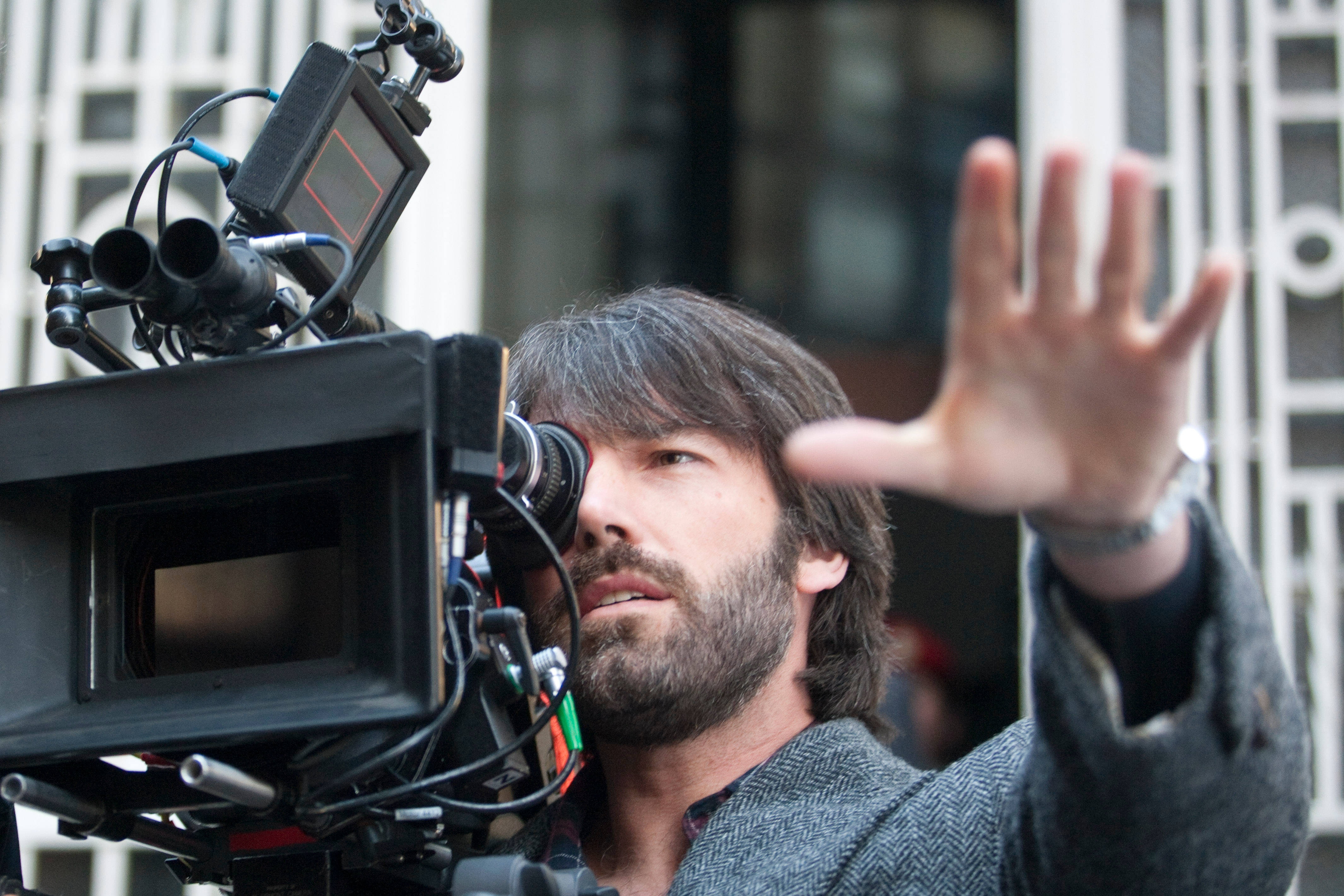 Ben Affleck 桌布 壁紙 — 一位留鬍鬚的男子在城市的街道上舉手指揮，同時操作專業電影攝影機。