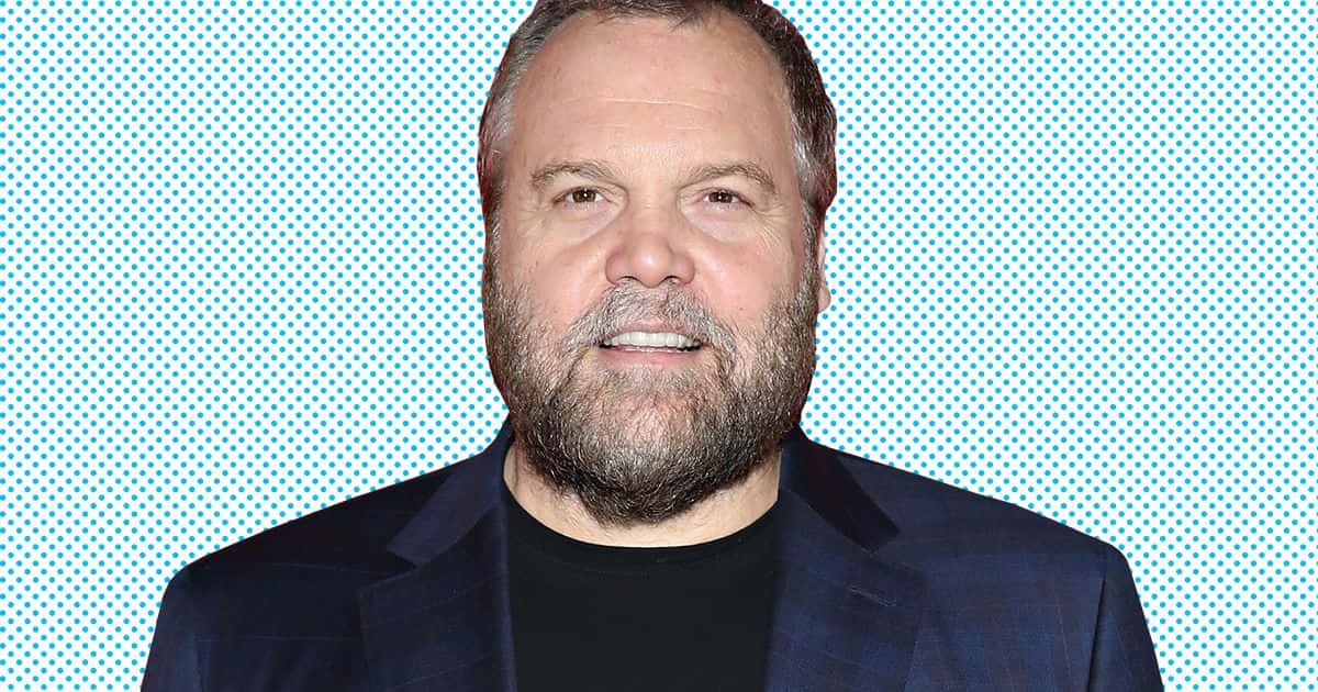 Vincent D'onofrio 桌布 壁紙 — 一位留鬍鬚的男子在明亮的藍色半色調背景前微笑，身穿黑色襯衫外搭深色西裝外套。