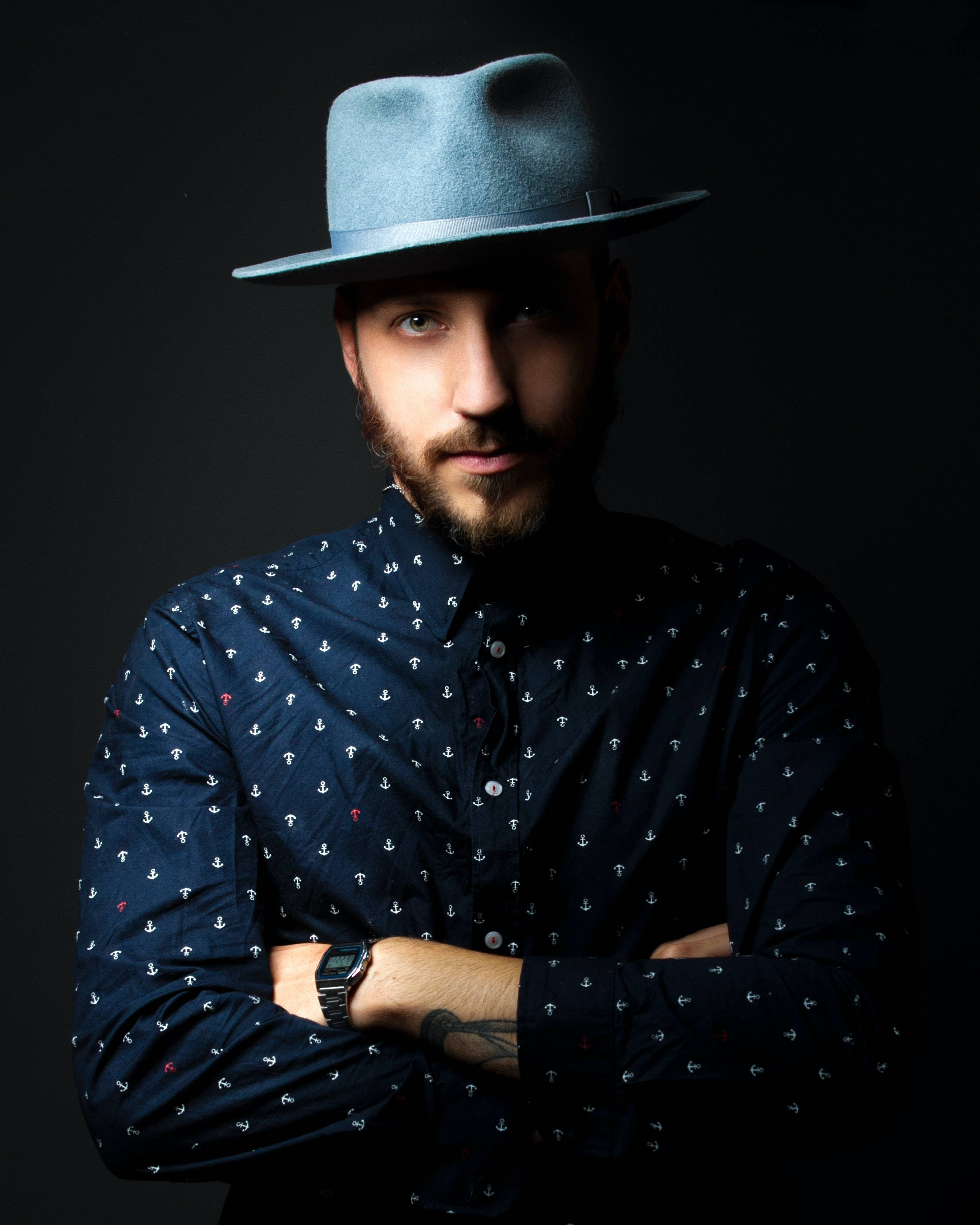 male model 桌布 壁紙 — 一位留鬍鬚的男子戴著藍色軟呢帽，自信地站在深色背景前，身穿海軍藍錨形圖案襯衫。