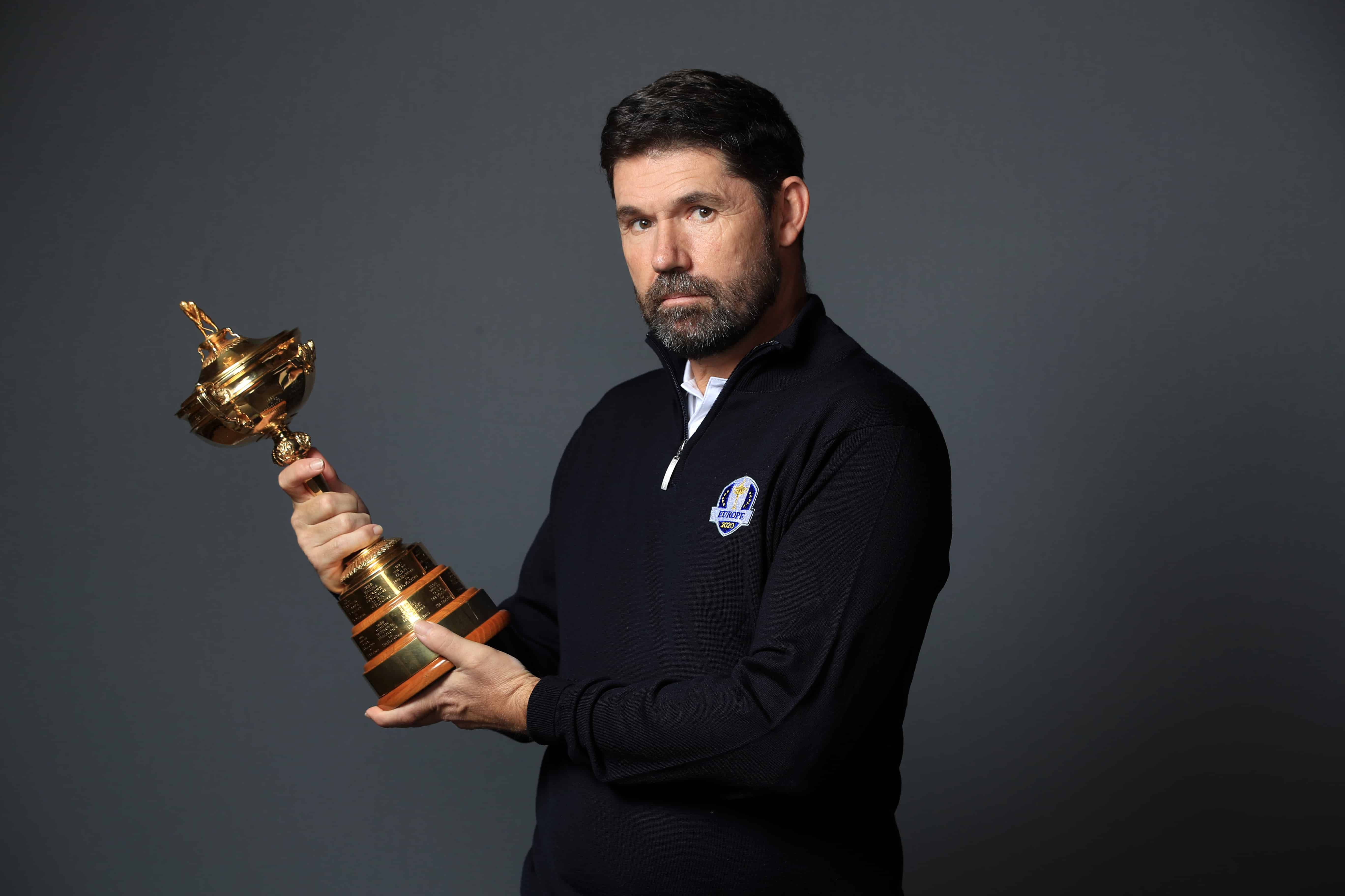 Trophy 桌布 壁紙 — 一位留鬍鬚的男子穿著深色Polo衫，在柔和的灰色工作室背景前手持閃閃發光的金色獎盃。
